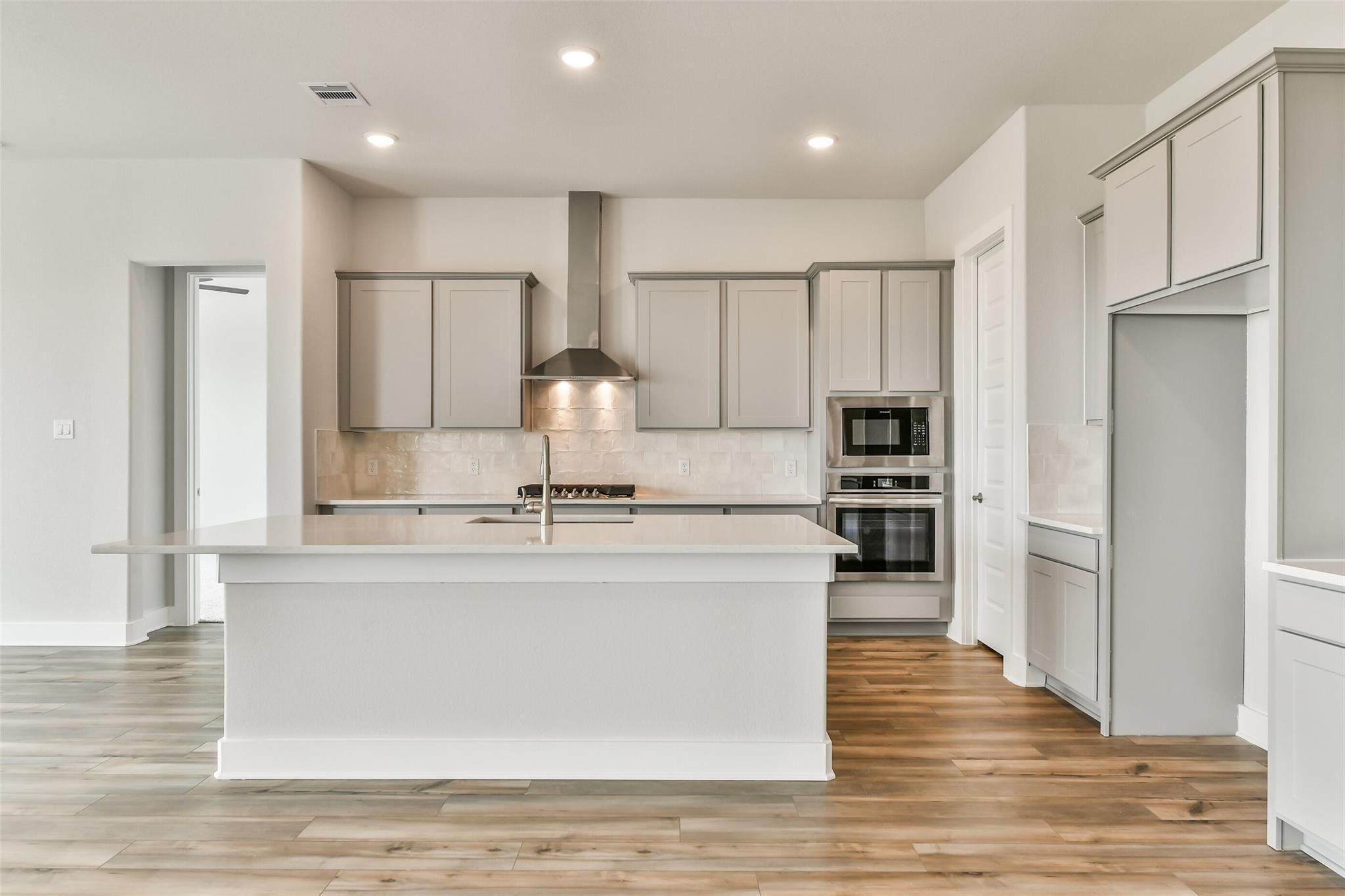 Modern kitchen with white quartz island, stainless steel appliances, and grey cabinets in Davidson Homes The George A, Lago Mar, Texas City