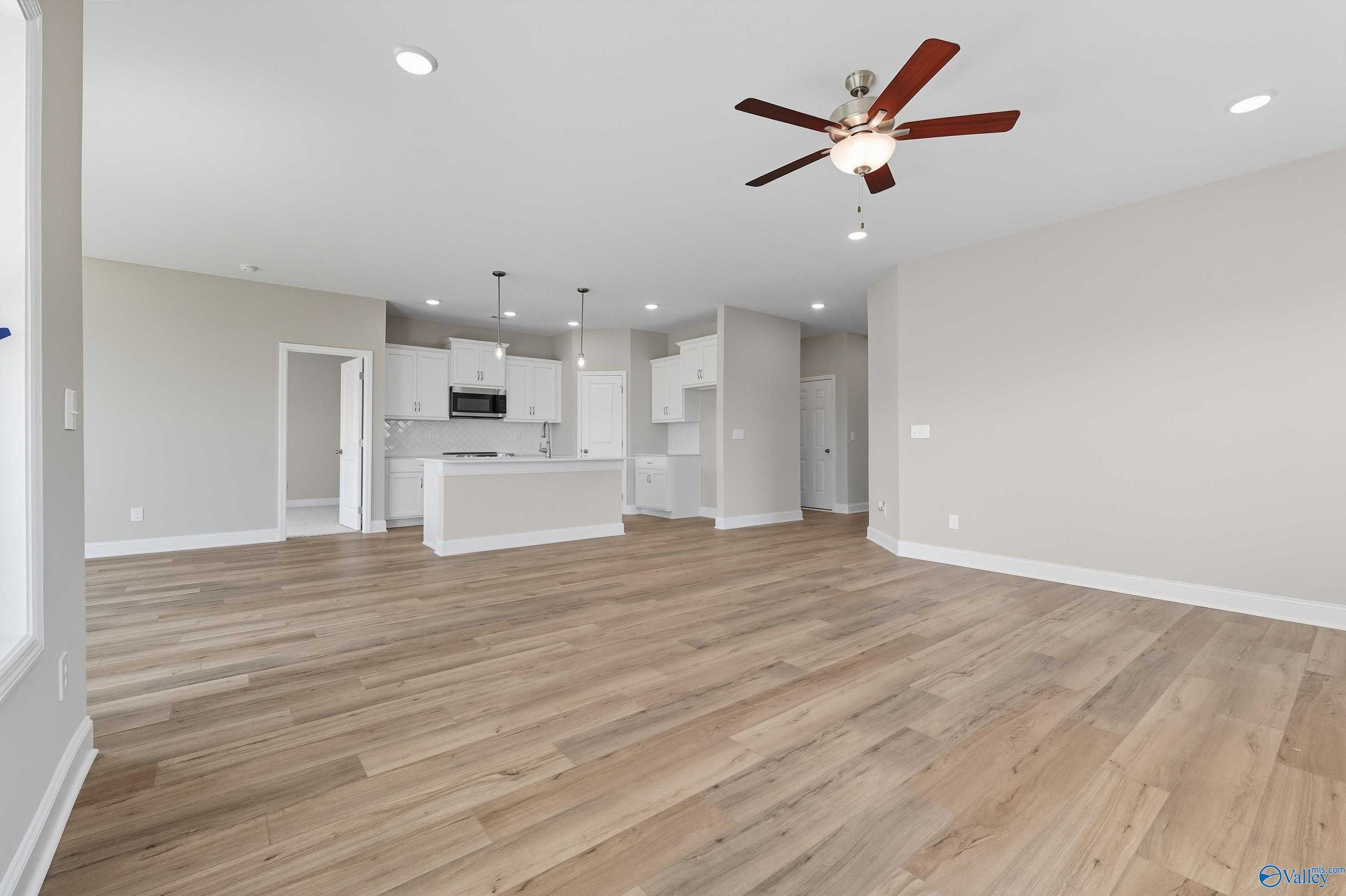 Open-concept kitchen and living area with white cabinets, island, ceiling fan, and hardwood floors in Davidson Homes The Franklin, Meridianville, AL