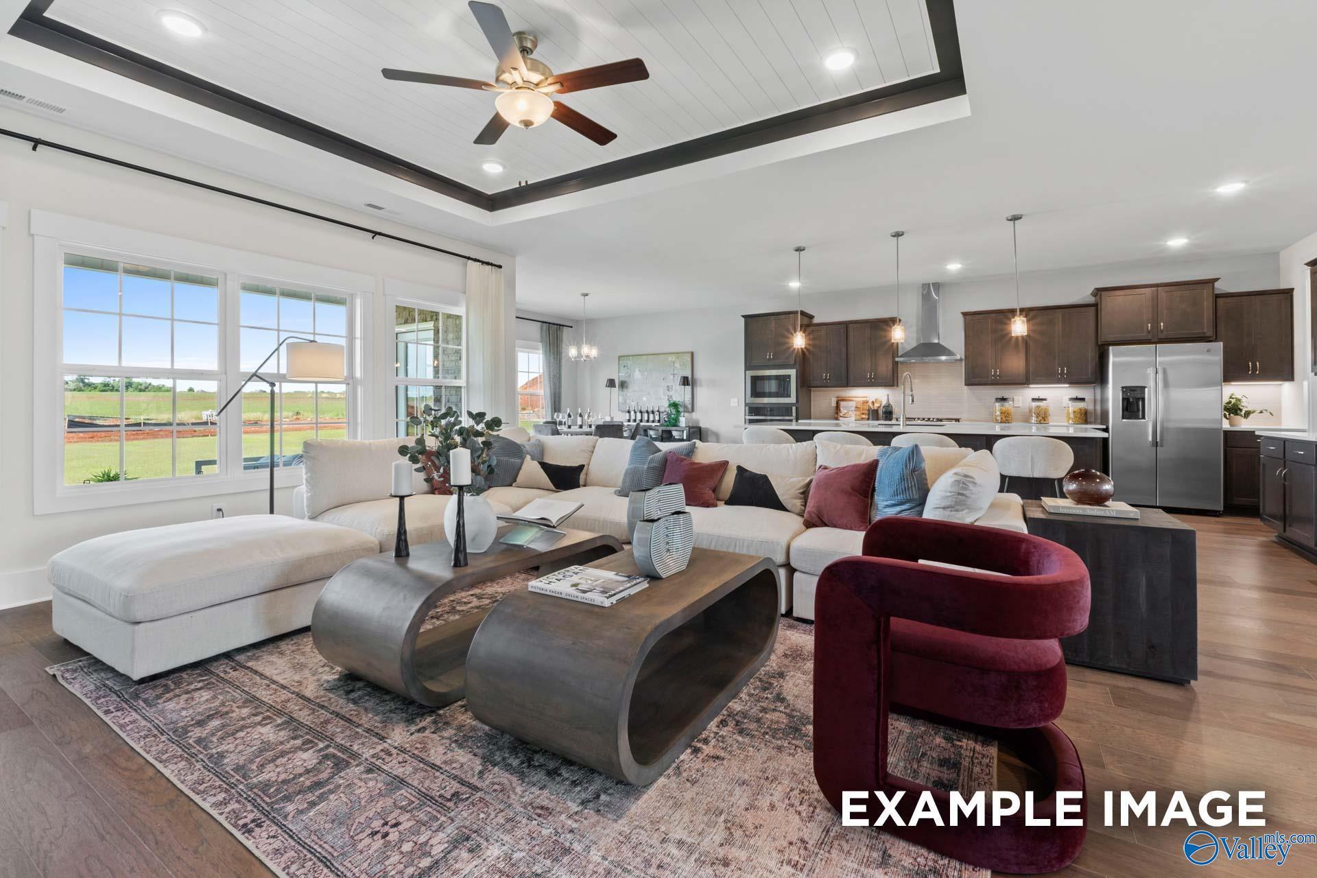 Modern open-concept living room with white L-shaped sofa, red armchair, dark wood tables, and kitchen views in The Finleigh, Huntsville, Alabama