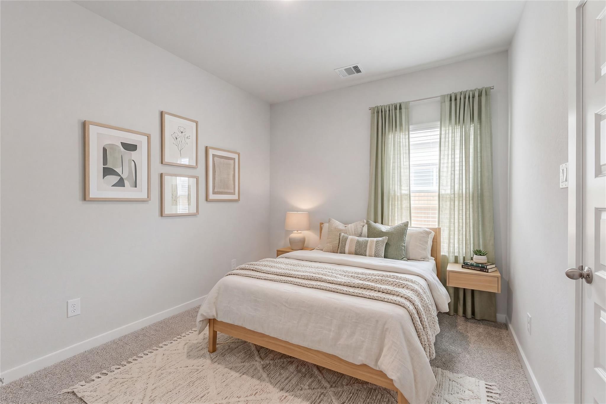 Cozy bedroom with light gray walls, wooden bed frame, green pillows, sheer curtains, and abstract wall art in Davidson Homes San Marcos H, Katy Texas