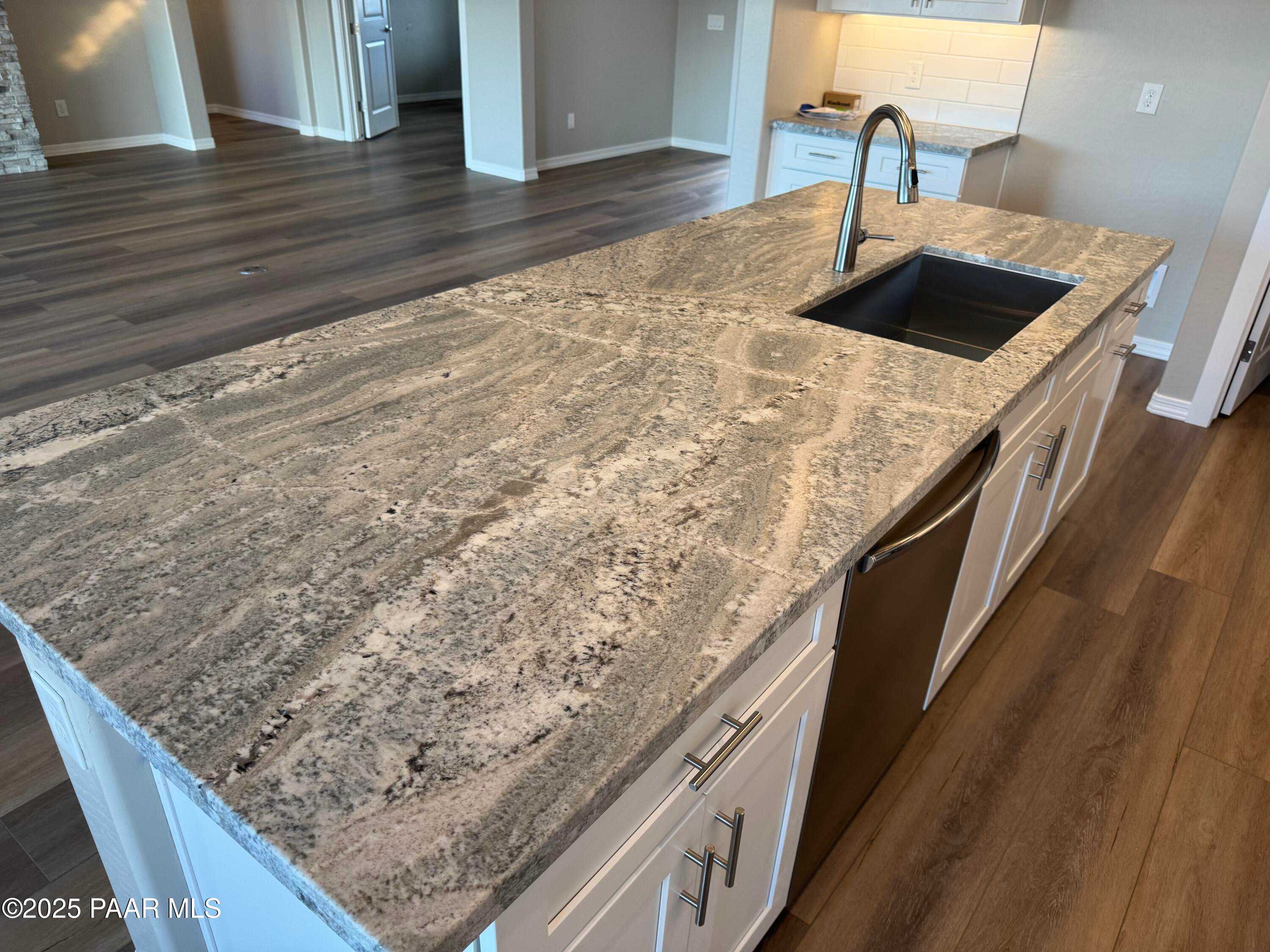 Modern kitchen island with veined granite countertop, stainless sink, dishwasher, white cabinets in Davidson Homes The Monarch A, Prescott AZ