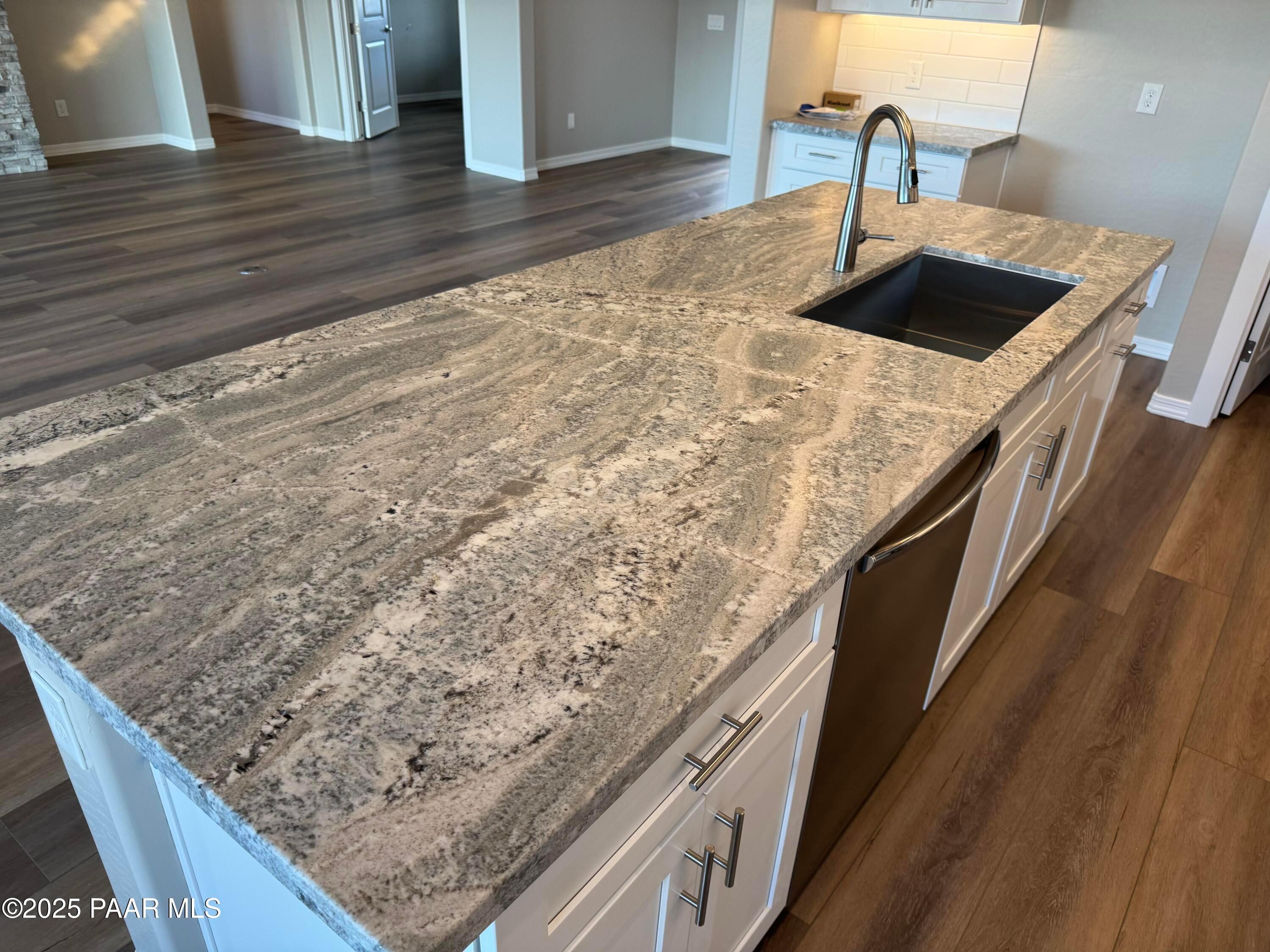 Modern kitchen island with veined granite countertop, stainless sink, dishwasher, white cabinets in Davidson Homes The Monarch A, Prescott AZ