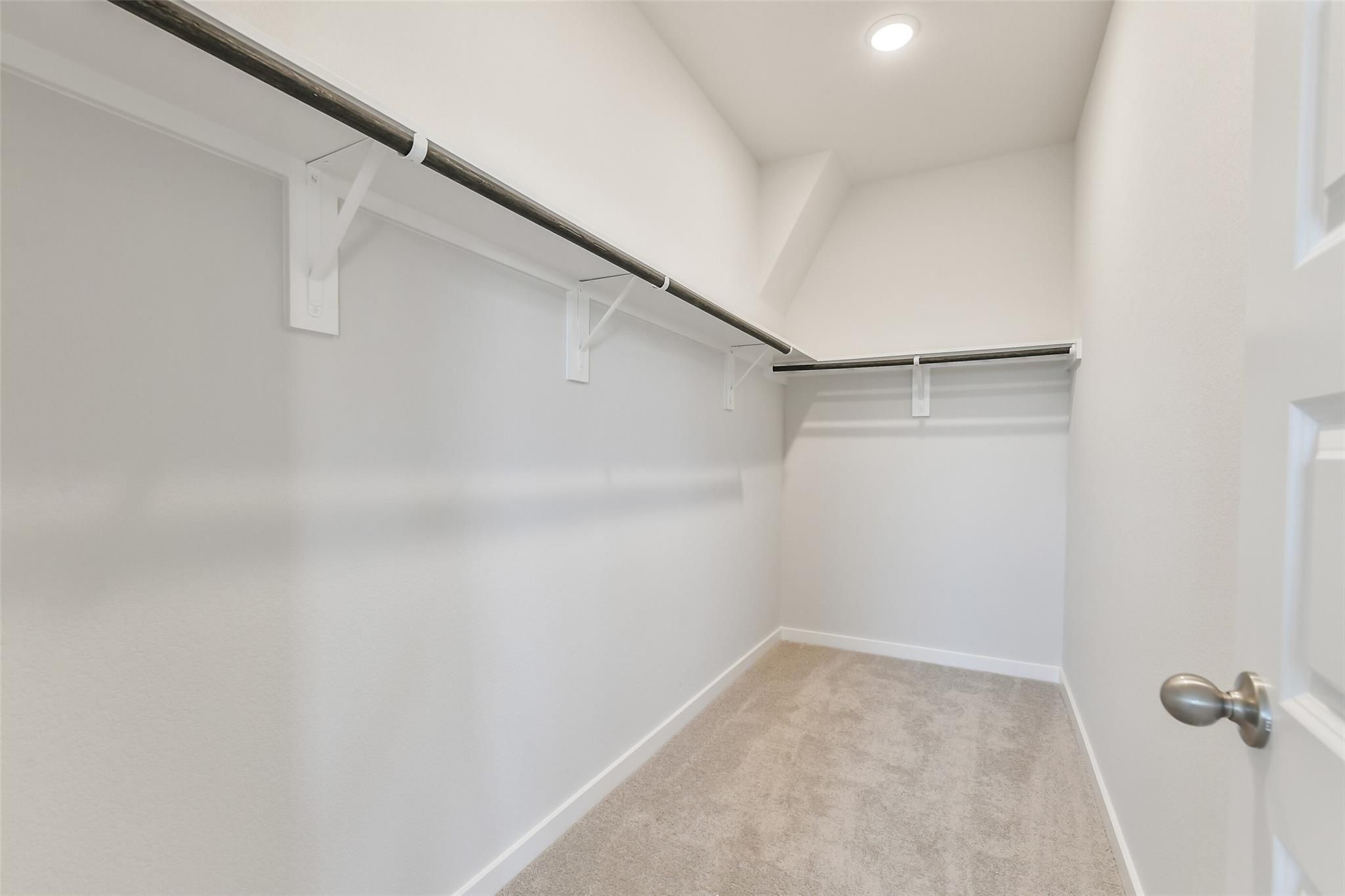 Spacious walk-in closet with double metal rods, white walls, and beige carpet in master suite of Davidson Homes The Colorado F, Cleveland, Texas