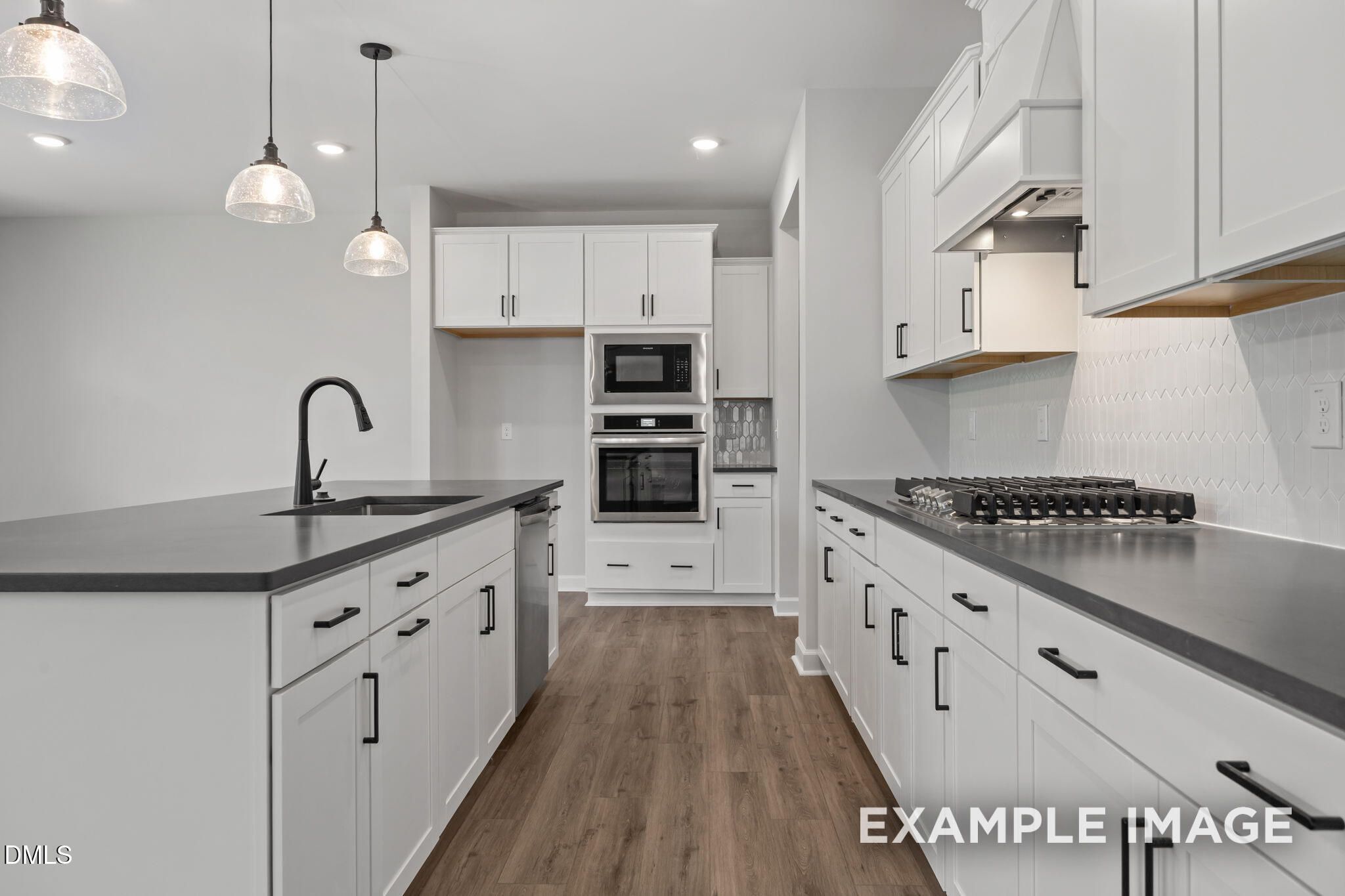 Modern kitchen with white shaker cabinets, dark countertops, stainless appliances, and pendant lights in Davidson Homes The Beech, Wendell Ridge