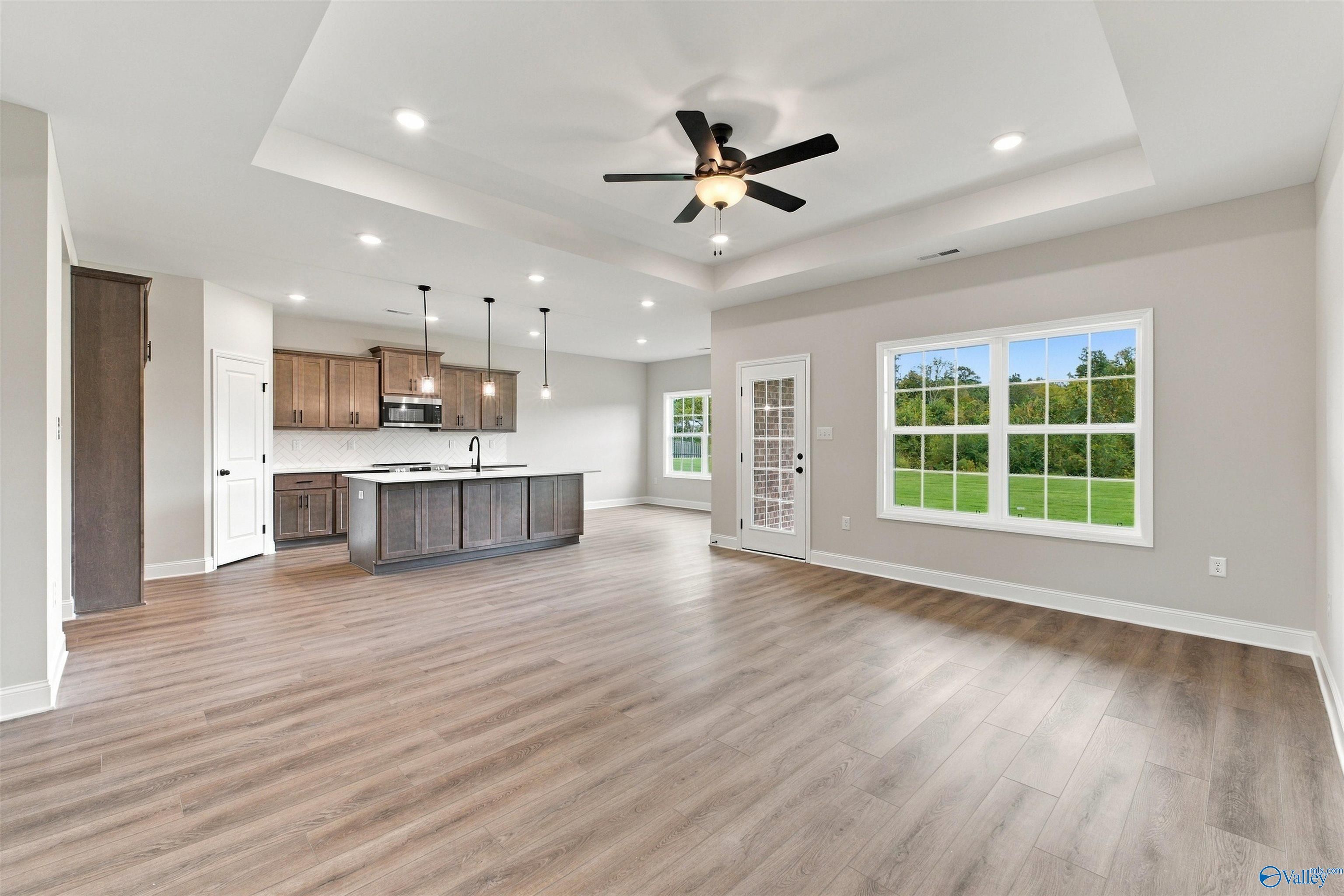 Open-concept living room and kitchen with wood floors, tray ceiling, and island in The Montgomery floor plan, Decatur, Alabama