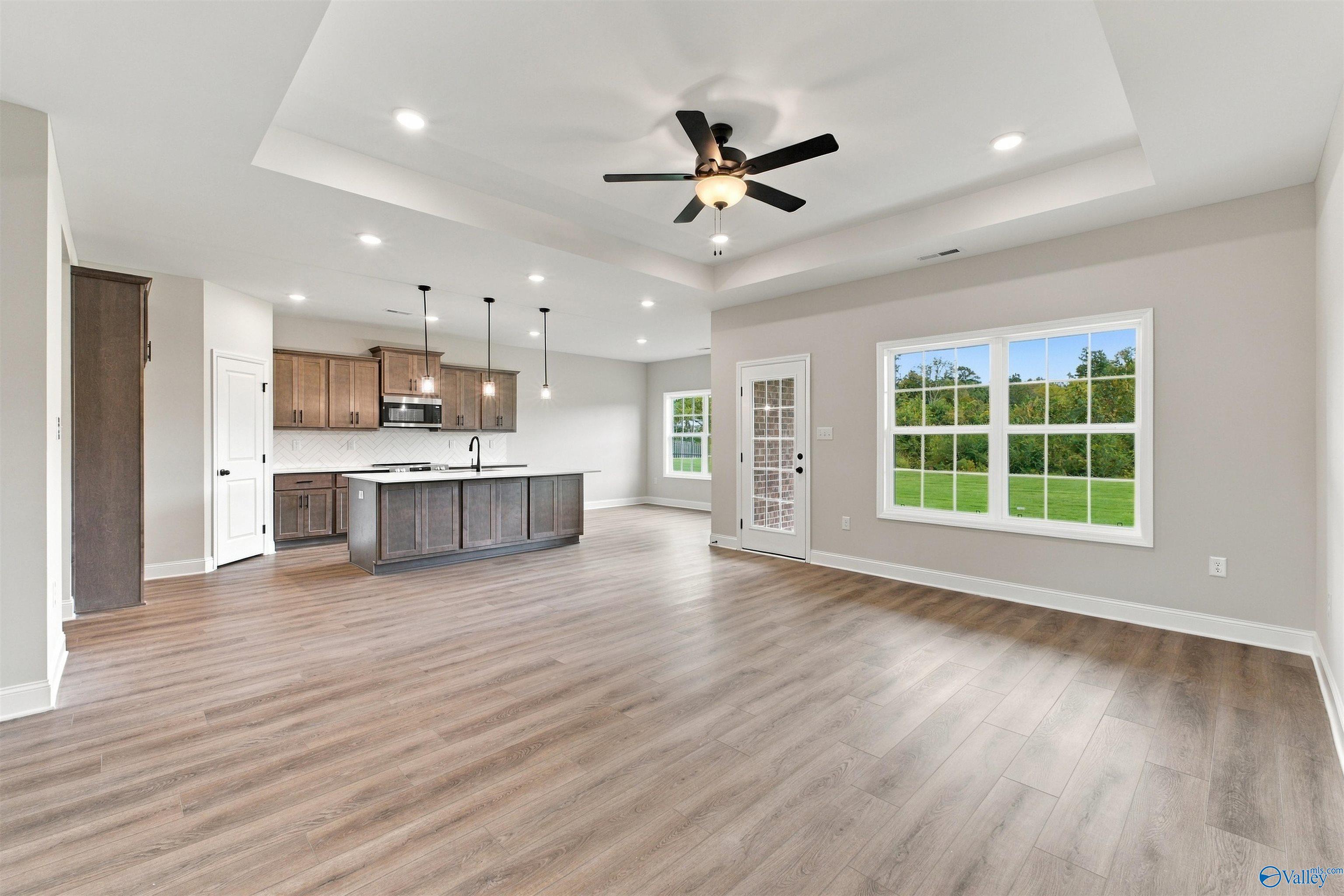 Open-concept living room and kitchen with wood floors, tray ceiling, and island in The Montgomery floor plan, Decatur, Alabama