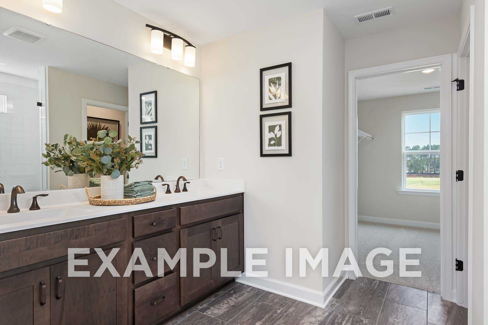 Modern master bathroom in The Willow F with double vanity, dark wood cabinets, large mirror, eucalyptus plant, and walk-in shower