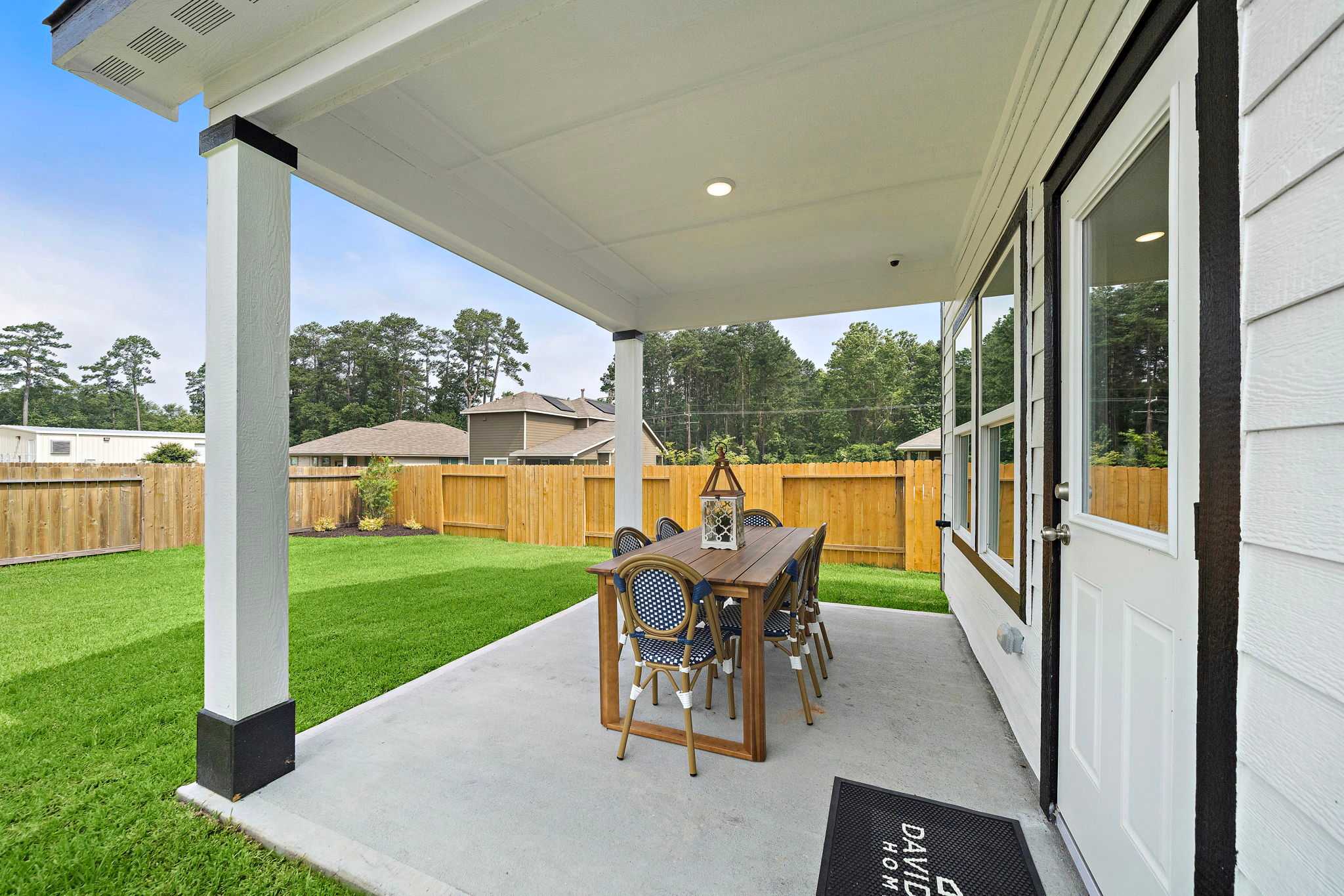 Covered patio at Liberty Estates in Cleveland Texas featuring wooden dining set, blue chairs, and lush green lawn by Davidson Homes