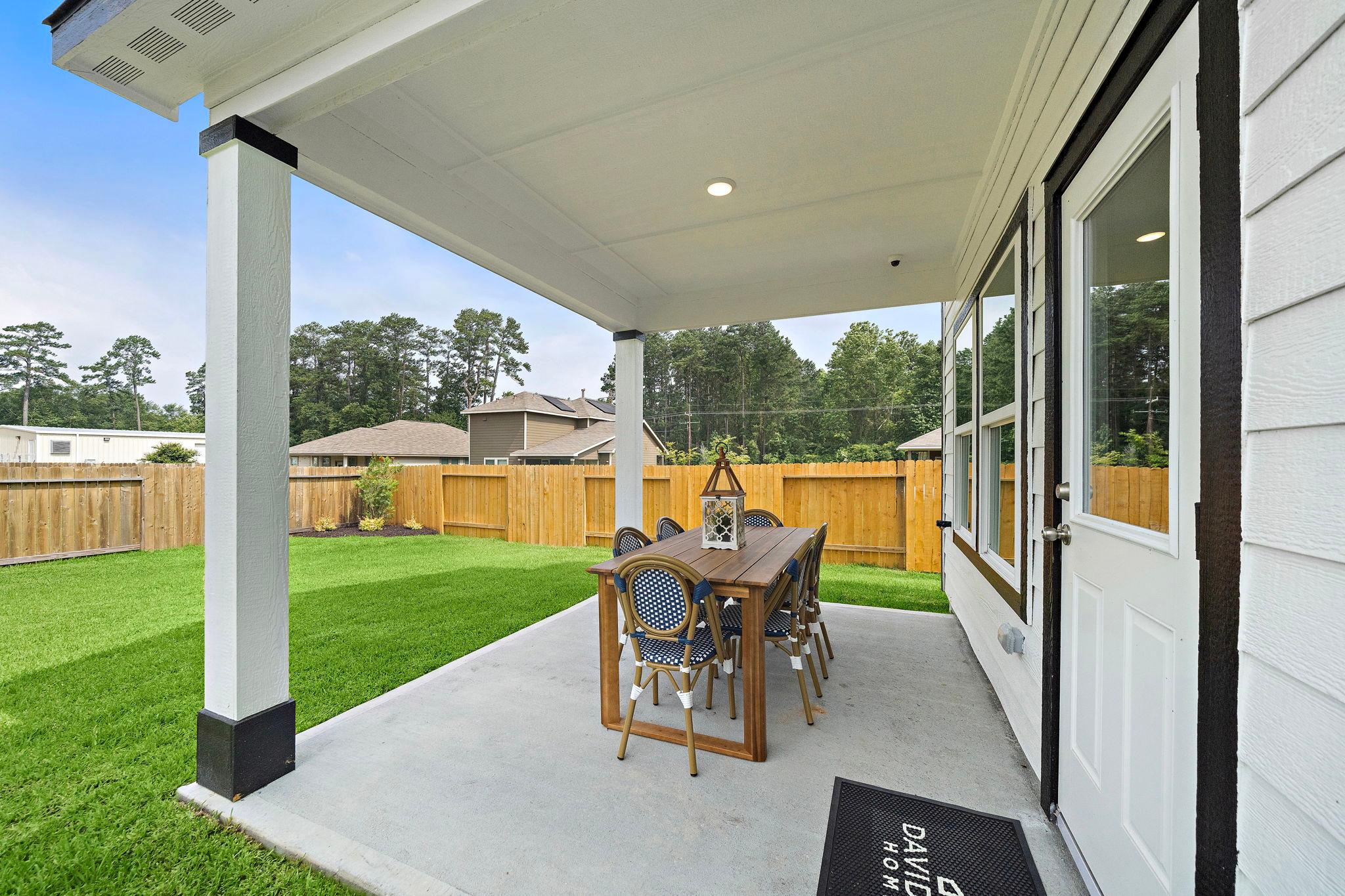 Covered patio at Liberty Estates in Cleveland Texas featuring wooden dining set, blue chairs, and lush green lawn by Davidson Homes