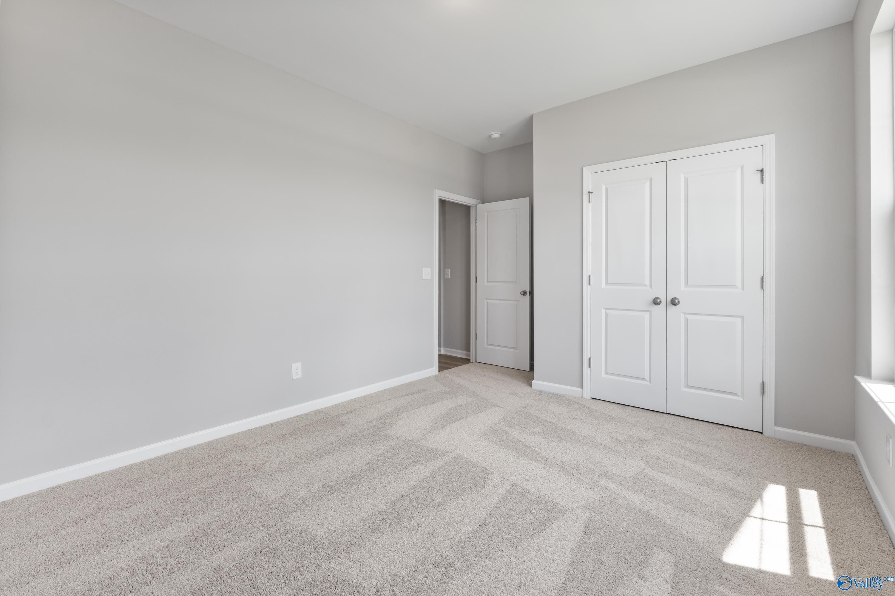 Empty bedroom featuring gray walls, white double closet doors, carpet floor, and natural light in Davidson Homes The Phoenix, Hazel Green AL