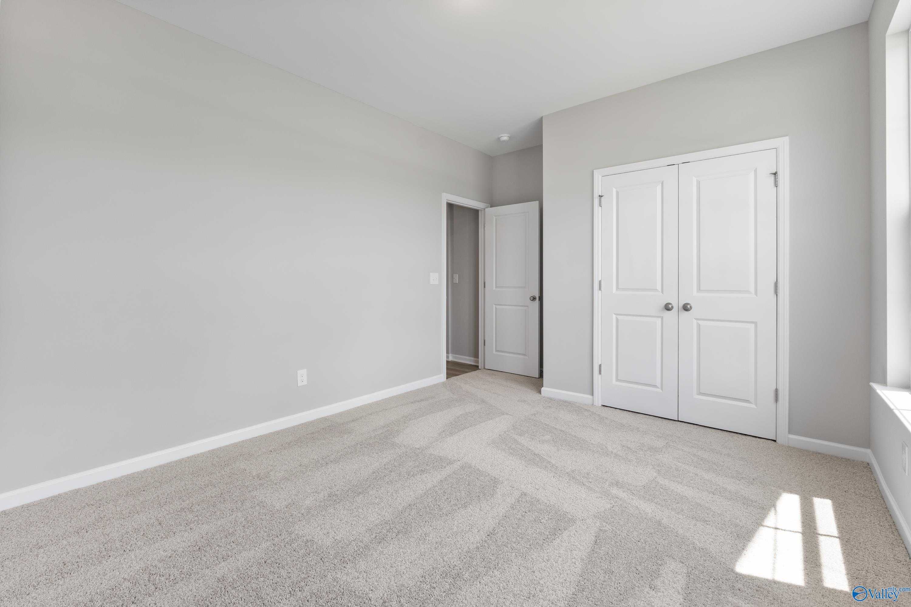 Bright secondary bedroom with double-door closet, gray walls, and plush carpet in Davidson Homes The Phoenix, Hazel Green, AL