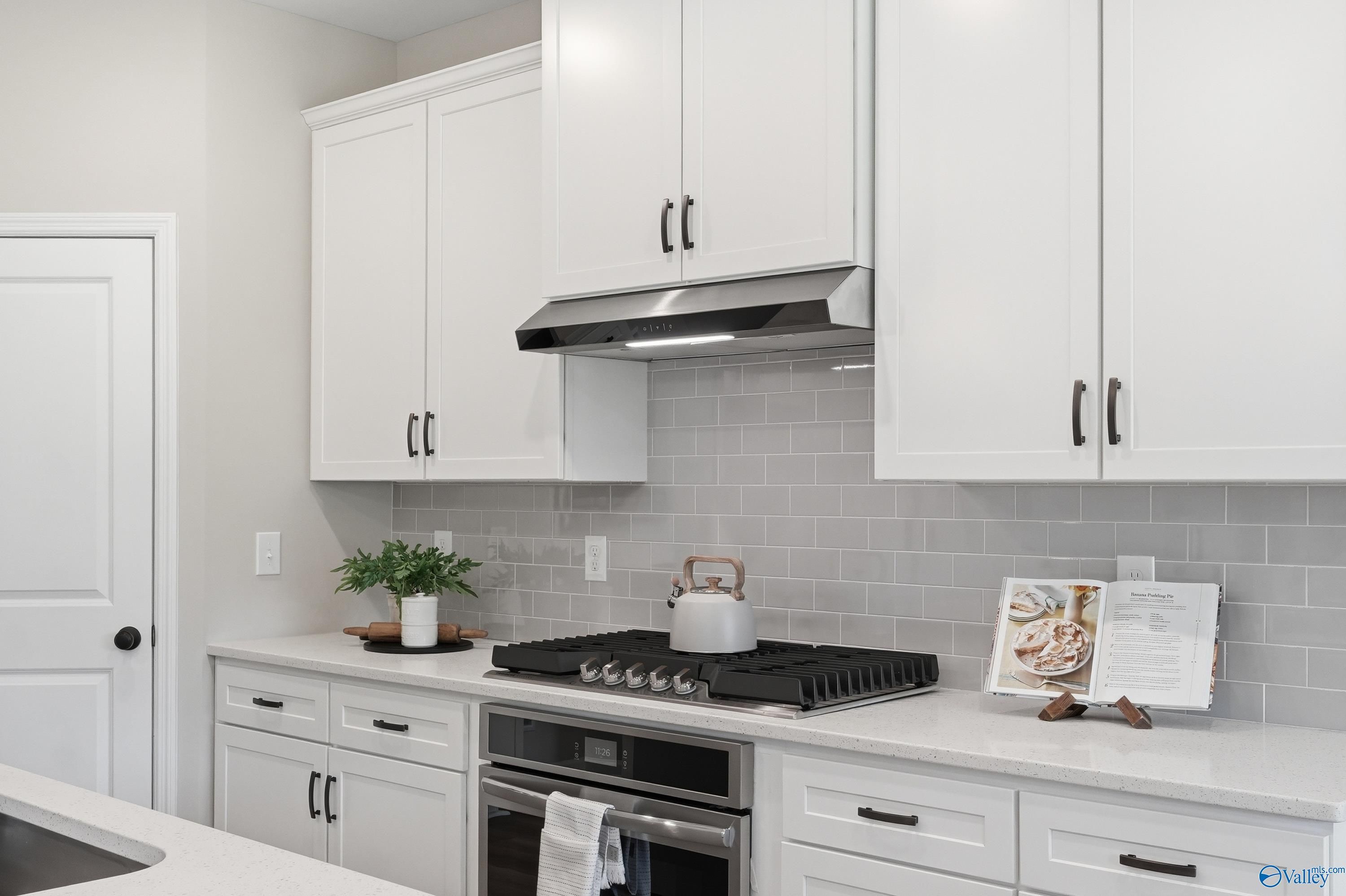 Modern white kitchen with shaker cabinets, quartz counters, gas range, stainless oven, gray subway tile in Davidson Homes The Dorado, Huntsville AL