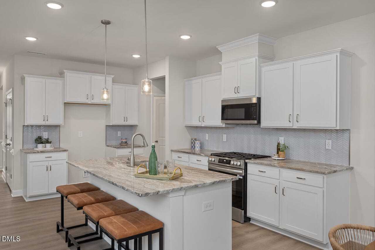 Modern white kitchen with quartz island, stainless appliances, pendant lights in Davidson Homes The Carter C, Lillington, NC