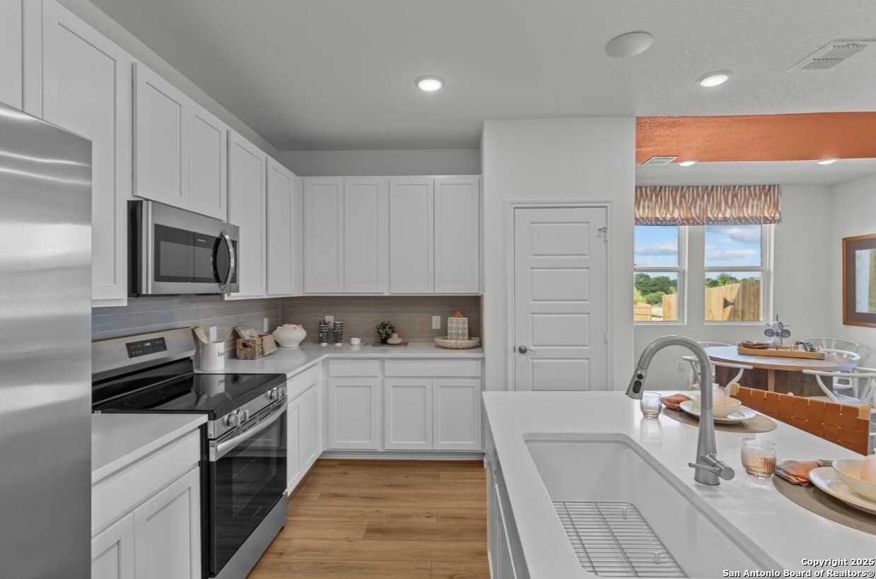 Modern white kitchen with stainless appliances, quartz island sink, and open dining in Davidson Homes Daphne J, Elmendorf, Texas
