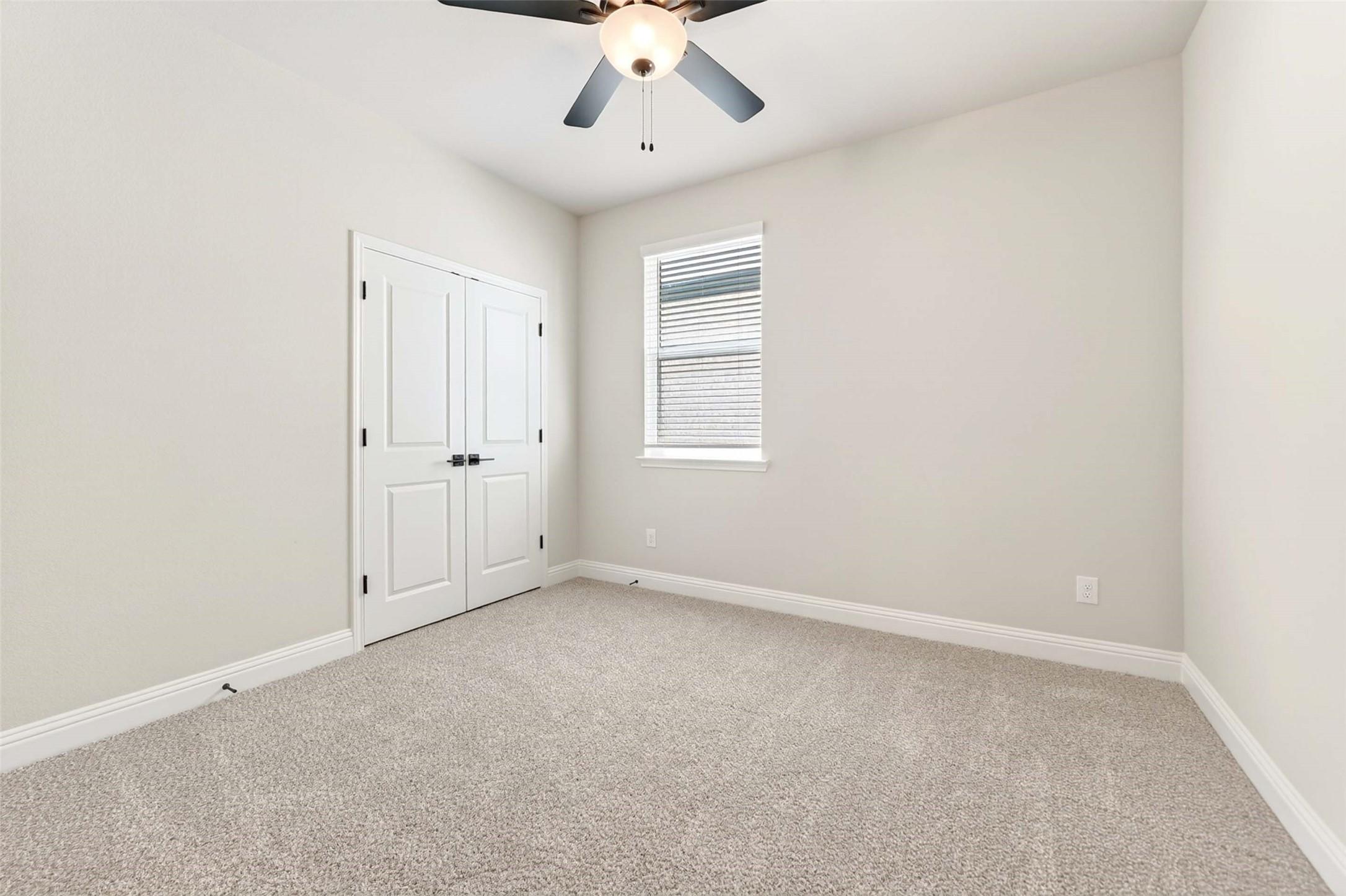 Bright secondary bedroom with plush carpet and ceiling fan in The Holly C floor plan, Parks at Foster Crossing, Anna, TX.