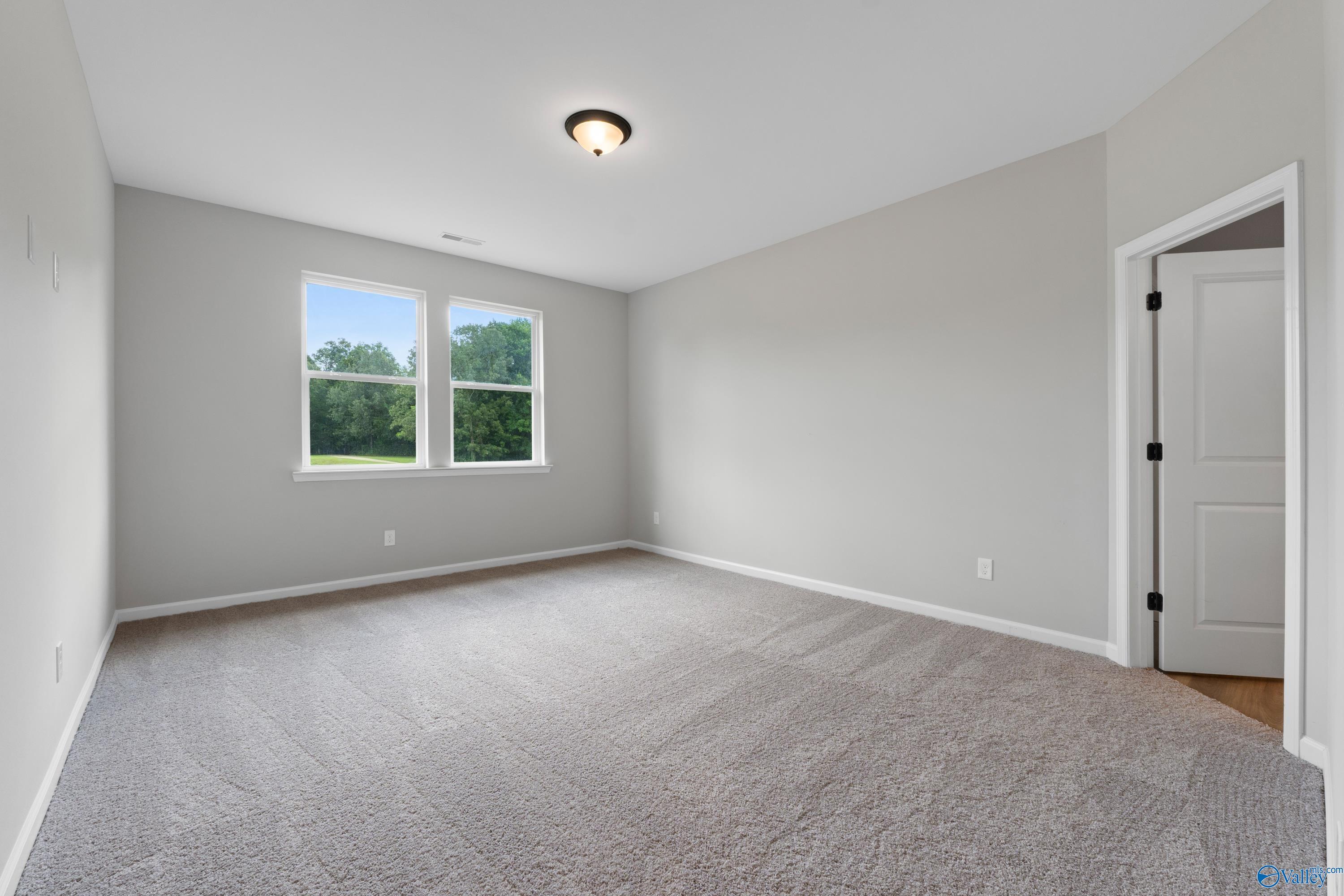 Empty secondary bedroom with light gray walls, carpet flooring, and large windows overlooking greenery in Davidson Homes The Dorado, Huntsville, AL