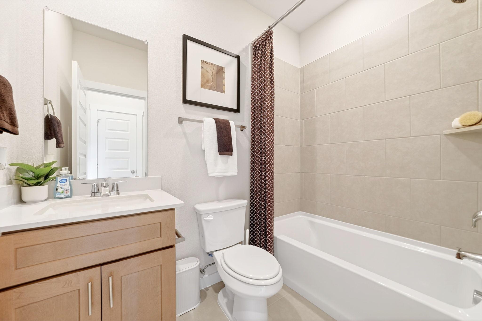 Cozy bathroom in Heartland Texas home by Davidson Homes with soaking tub, oak vanity sink, white toilet, and beige tile walls