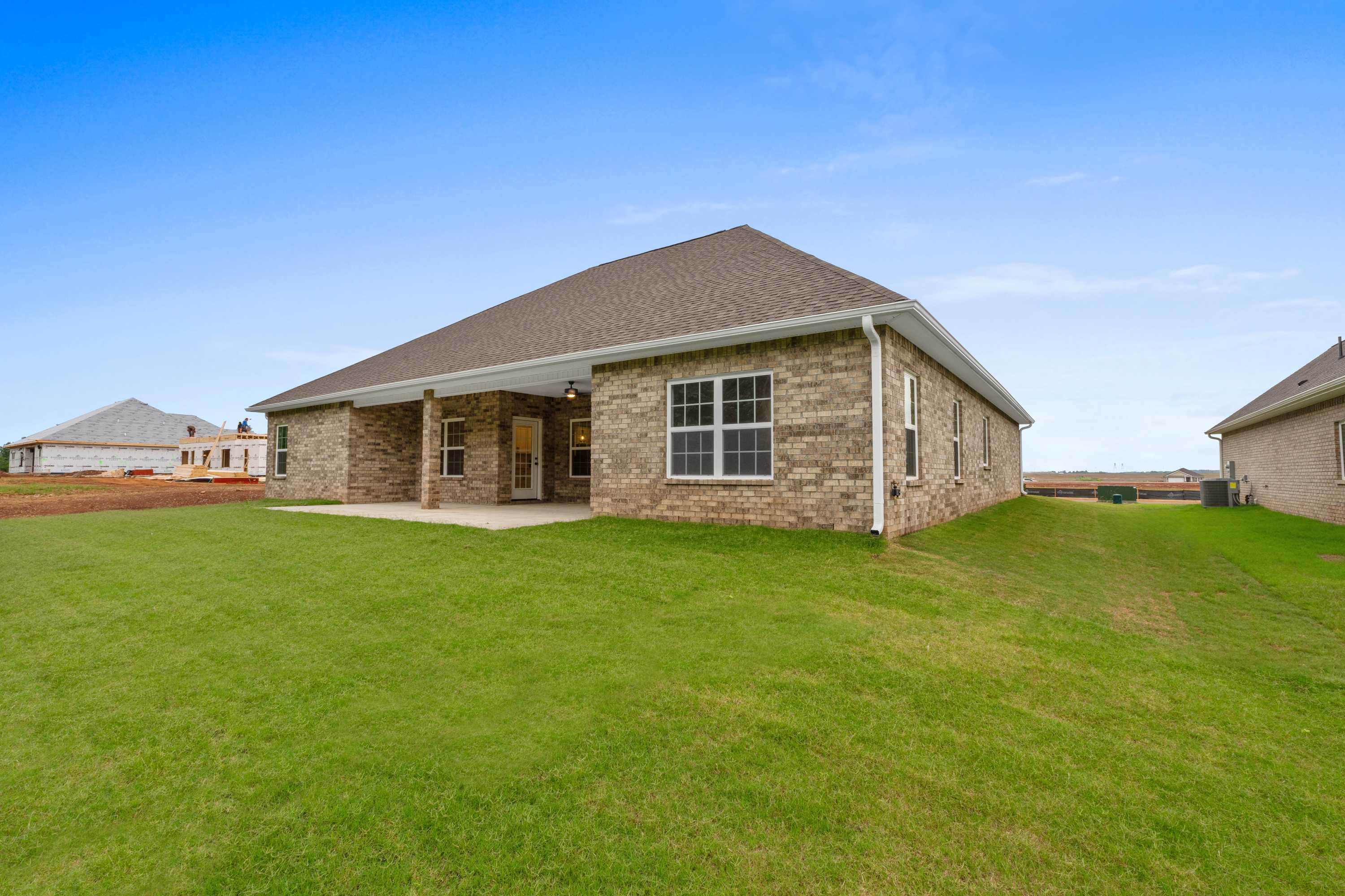 Side view of The Oxford 1-story brick home with shingle roof, covered porch, large windows, and green lawn in Meridianville