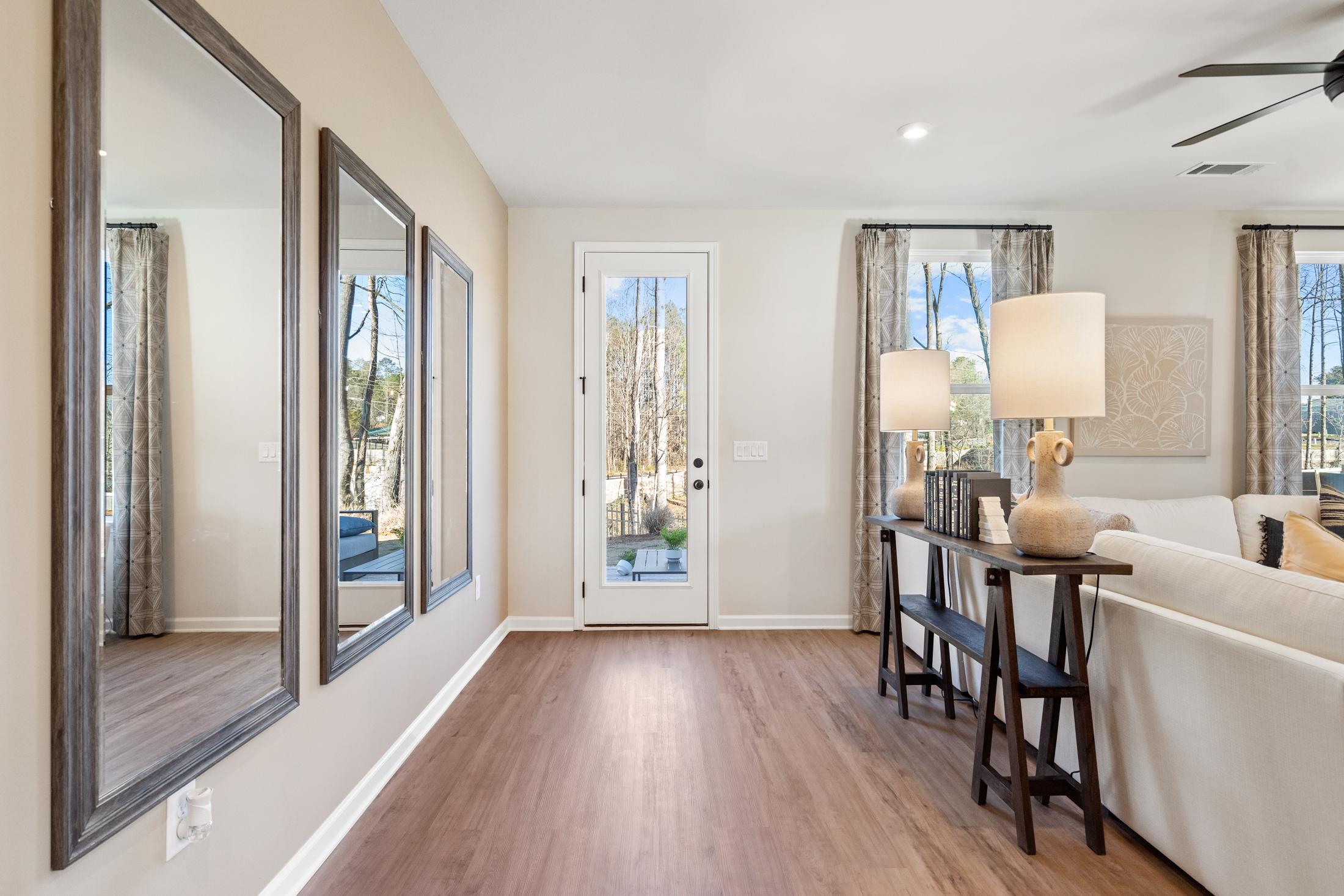 Spacious living room in The Marion A home with large wall mirrors, hardwood floors, and French door view of trees