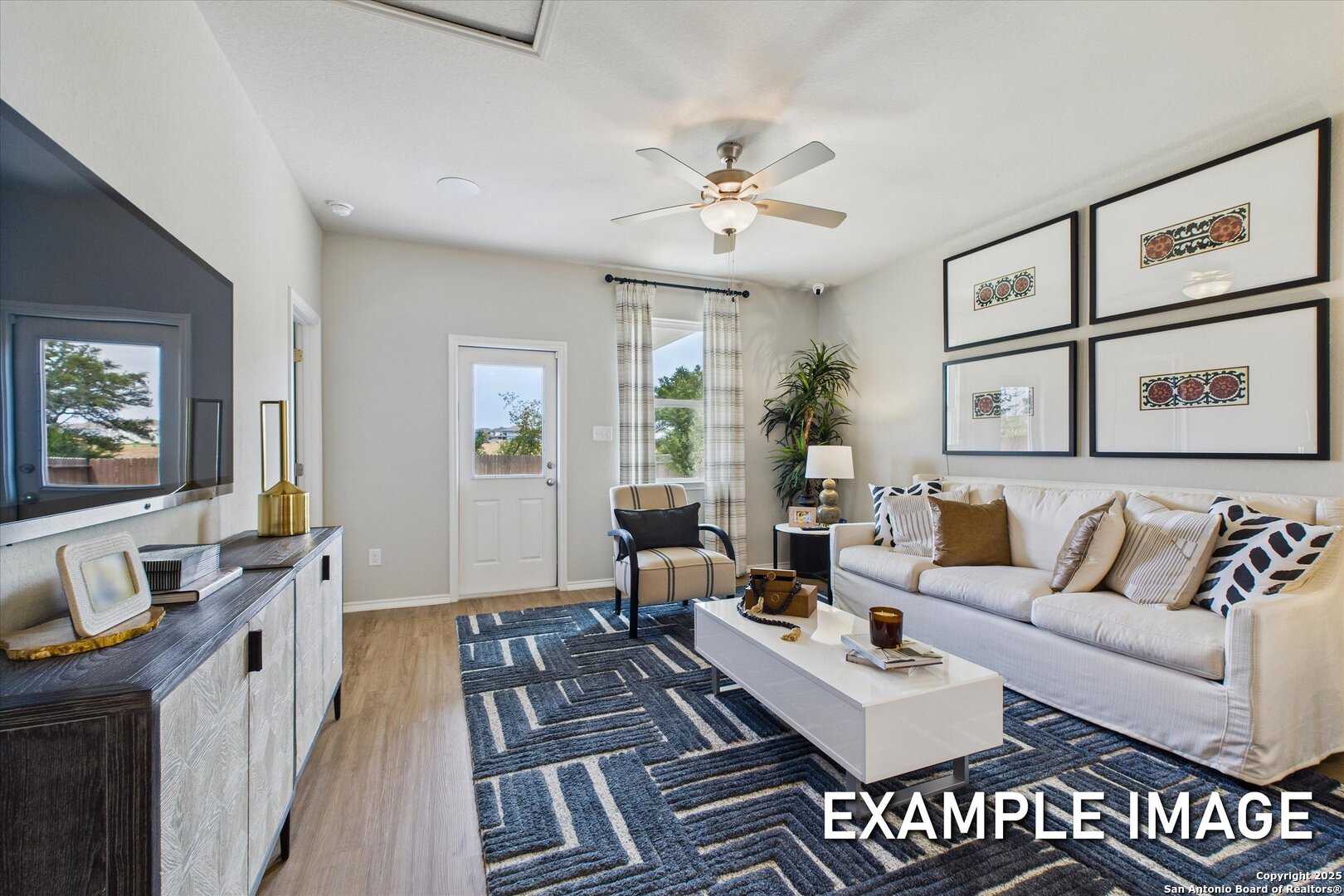 Cozy living room with white sofa, ceiling fan, wall-mounted TV, sliding glass door, and hardwood floors in Davidson Homes The Sabine C, San Antonio