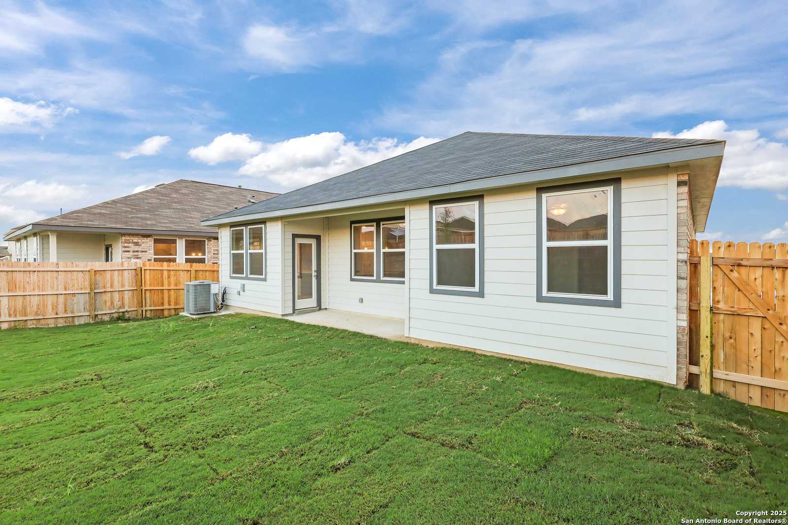 Back view of The Asheville J single-story home by Davidson Homes, beige siding, large windows, green lawn, wooden fence in Comanche Ridge, San Antonio, Texas