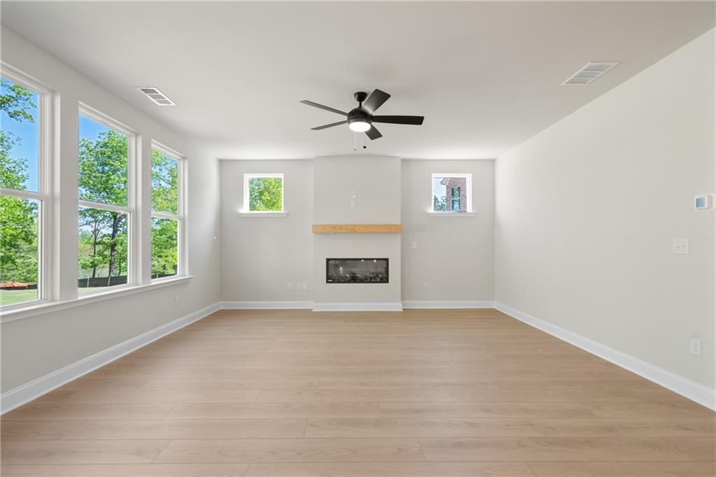 Bright family room with gas fireplace, hardwood floors, ceiling fan, and large windows overlooking trees in The Hickory E, Buford GA