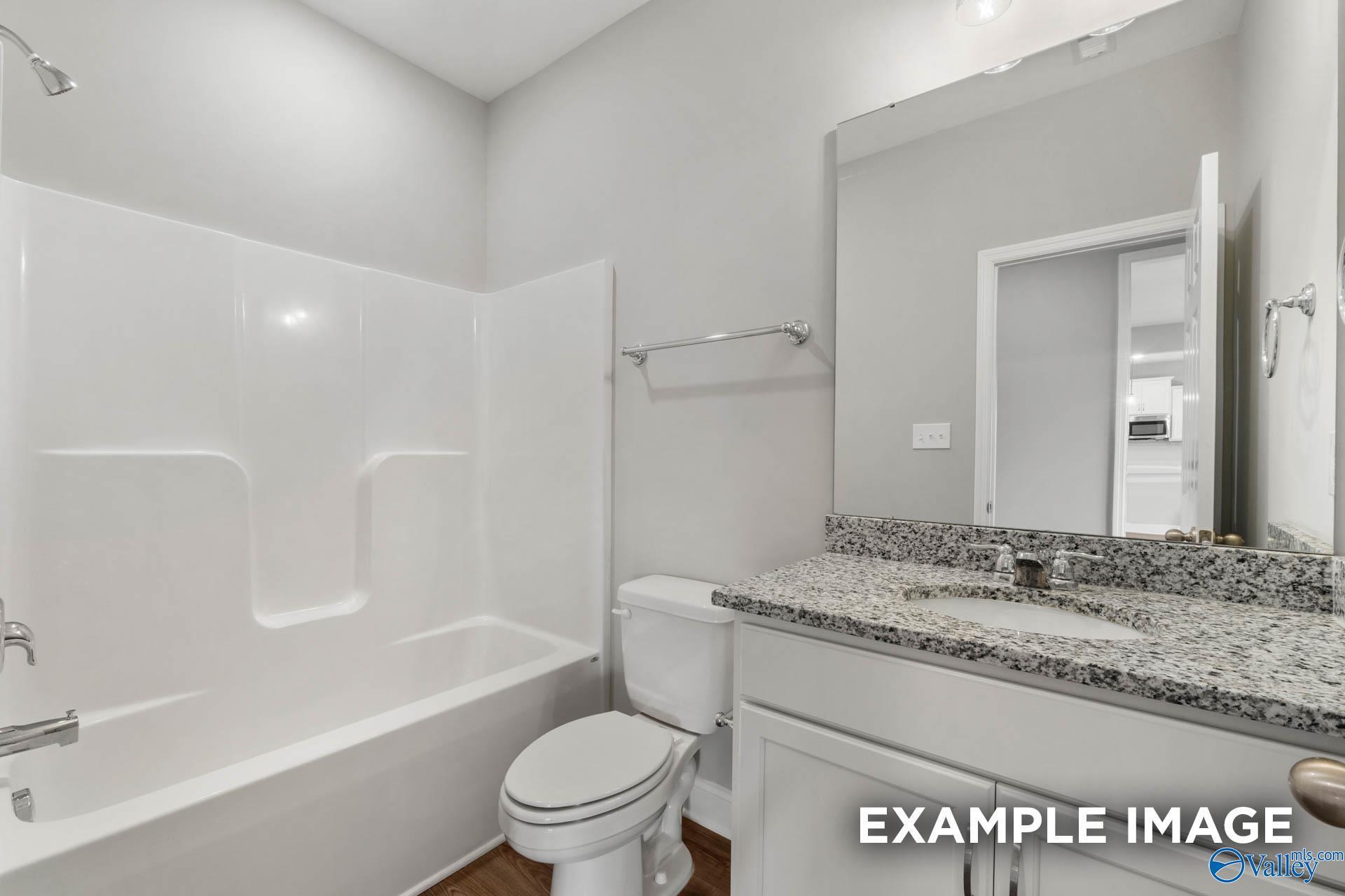 Modern bathroom featuring granite vanity, white tub-shower combo, and toilet in Davidson Homes The Shelby B, New Market, Alabama