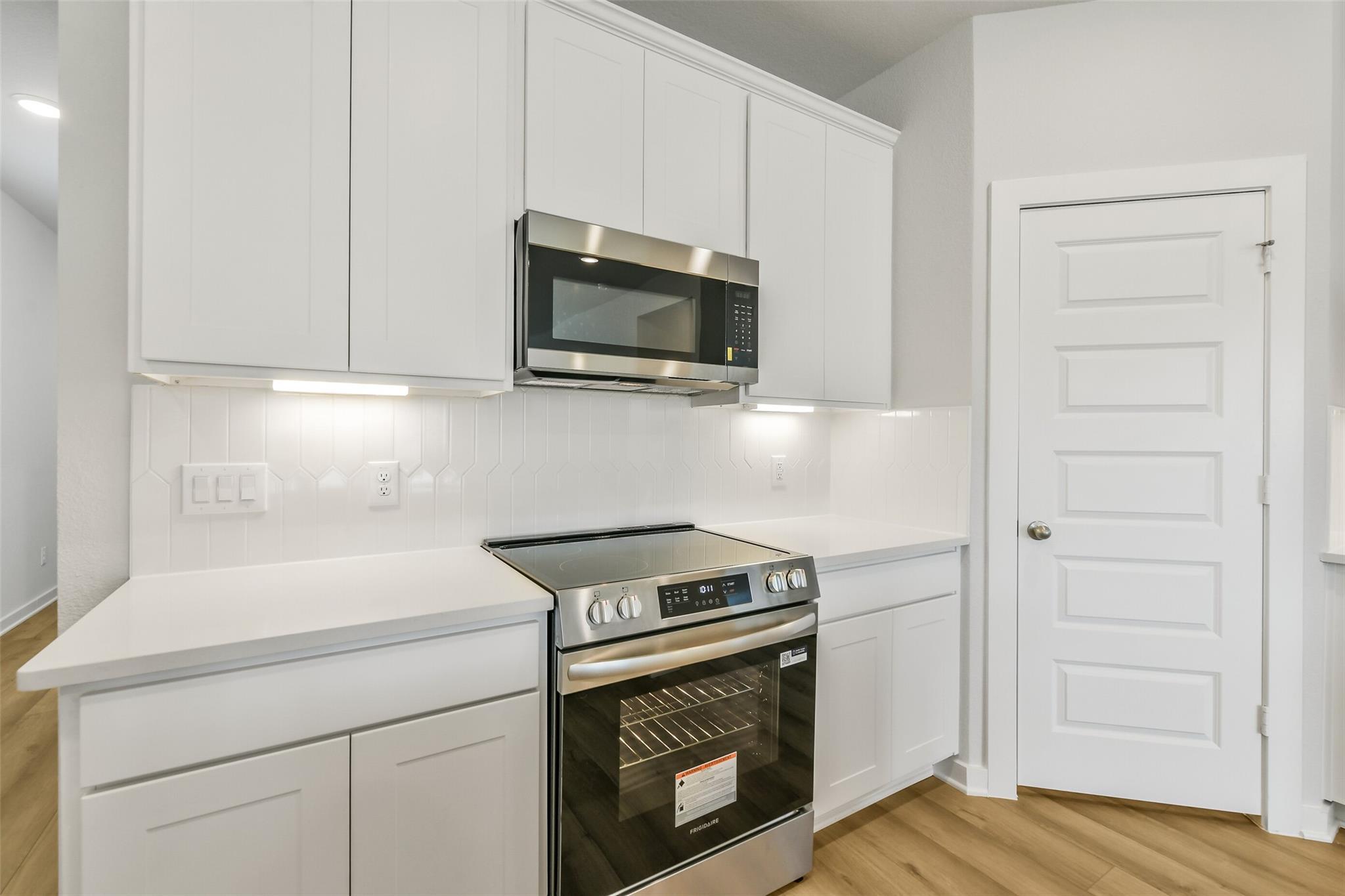 Modern white shaker kitchen with stainless steel microwave, range, and quartz counters in The San Marcos E, Cleveland, TX