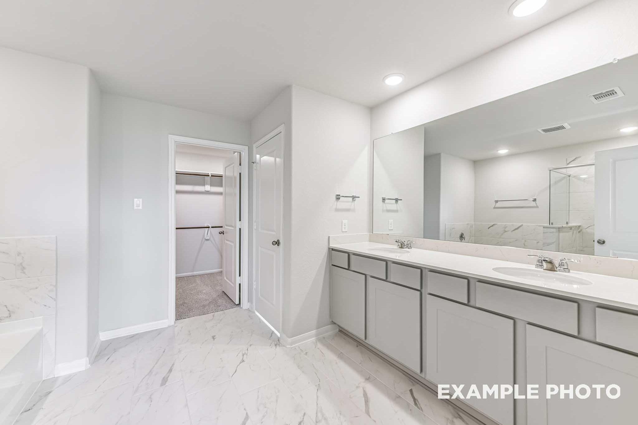 Spacious master bathroom in The Laguna A with double vanity, marble counters, large mirror, and walk-in closet access