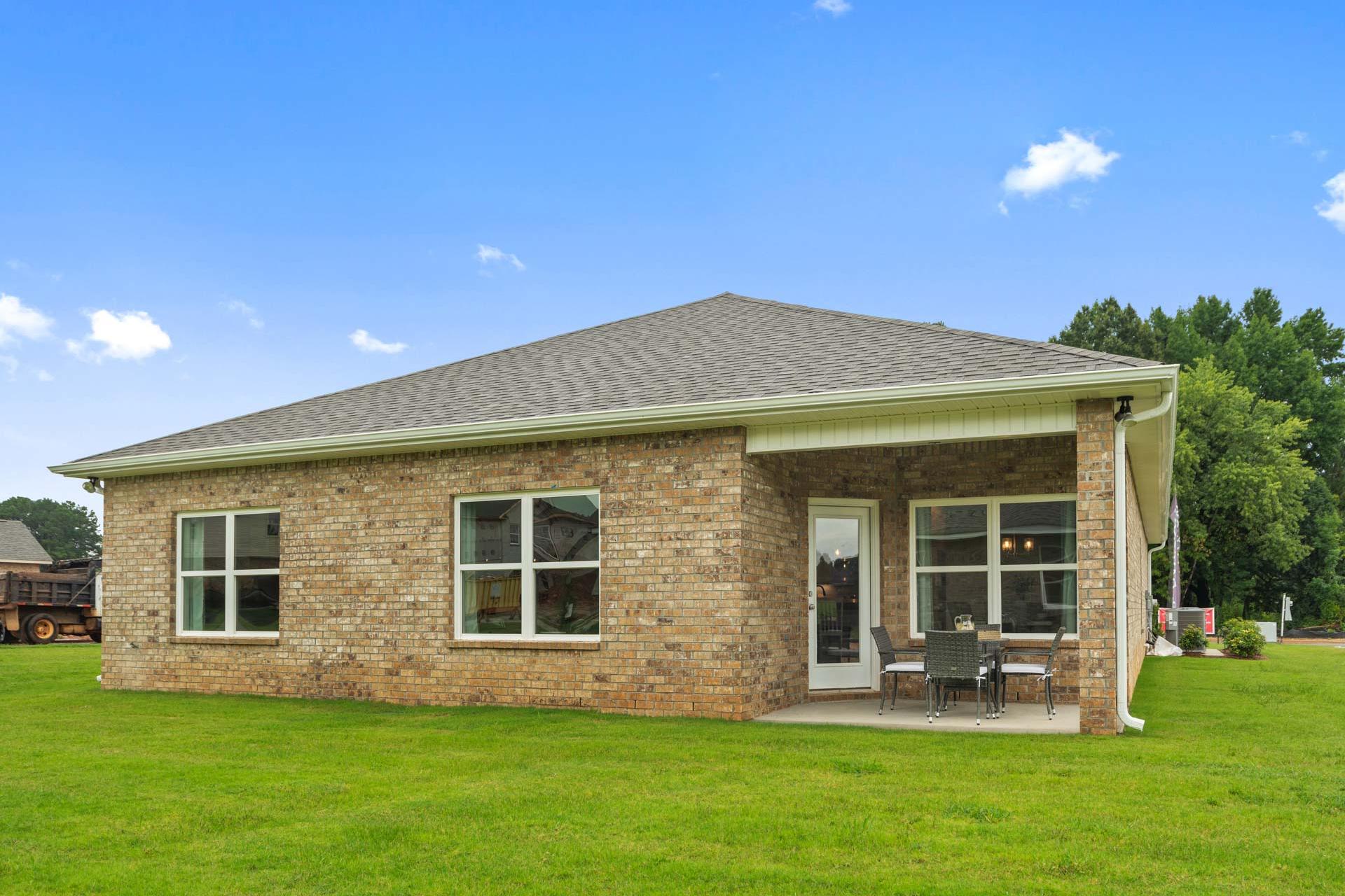 Single-story brick home exterior at Durham Farms in Harvest, Alabama with covered porch, chairs, and lush green lawn
