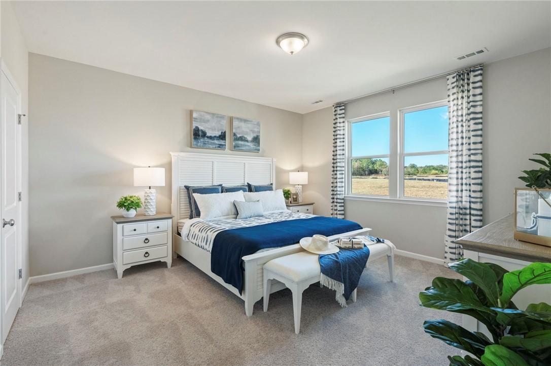 Elegant master bedroom with white king bed, blue bedding, large sunny windows, plants in Davidson Homes The Phoenix B, Opelika, Alabama