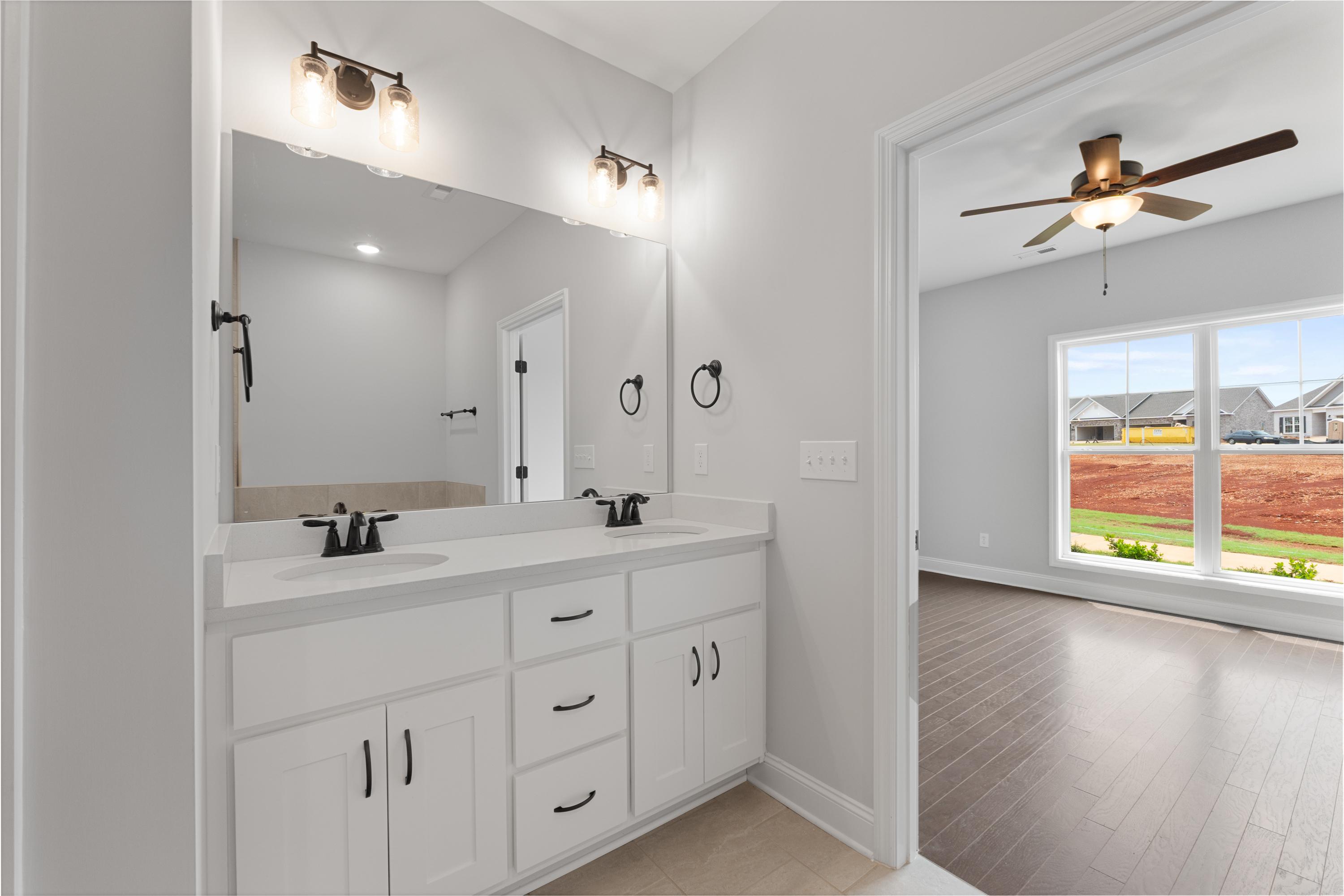 Spacious master bathroom in The Copeland with double white vanity, bronze fixtures, and adjacent bedroom view