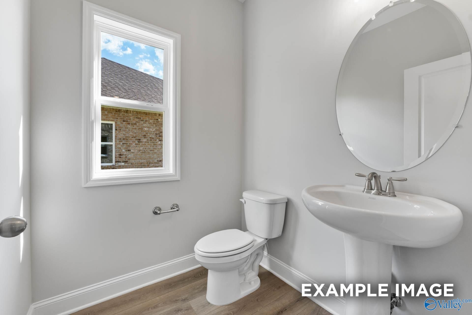 Elegant powder room featuring white pedestal sink, round mirror, and window in Davidson Homes The Chelsea D, New Market, Alabama