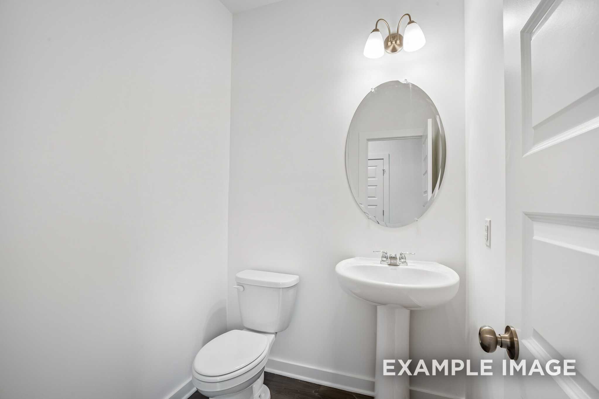 Bright powder room in The Grayson C with white pedestal sink, round mirror, toilet, and brass fixtures