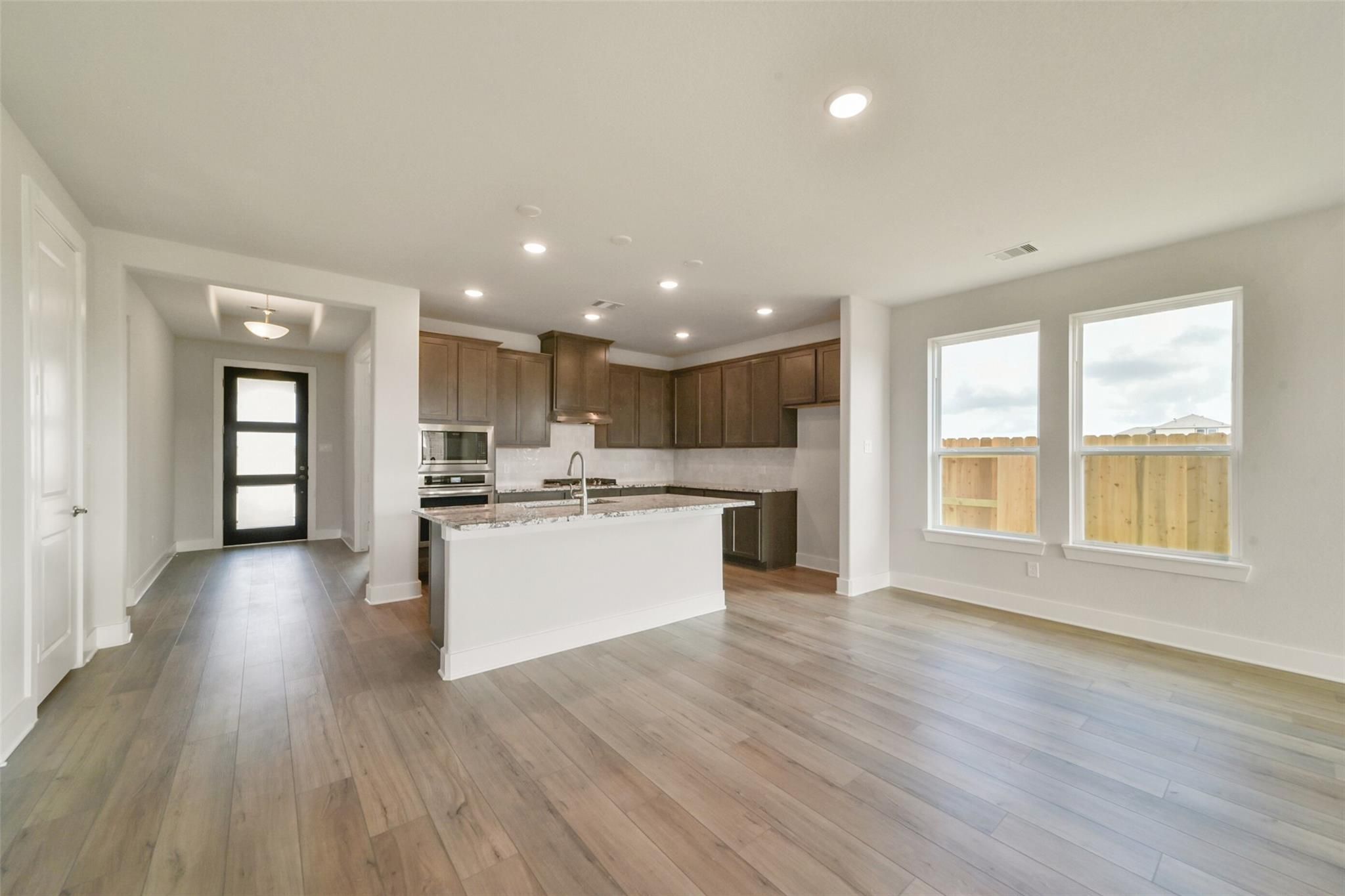 Open-concept kitchen with white island, stainless appliances, wood floors in Davidson Homes The Zion A, Lago Mar, Texas City