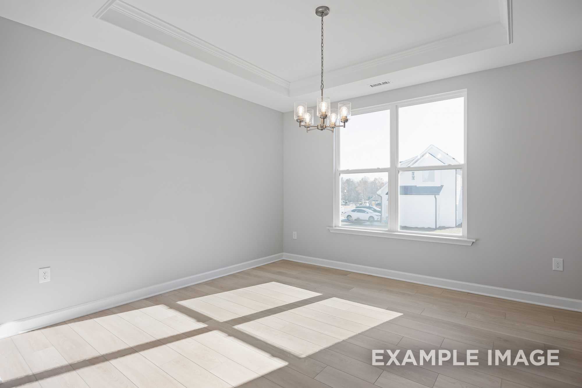 Spacious empty dining room in The Cypress D II with gray walls, tray ceiling, chandelier, large window, and hardwood floors bathed in natural light