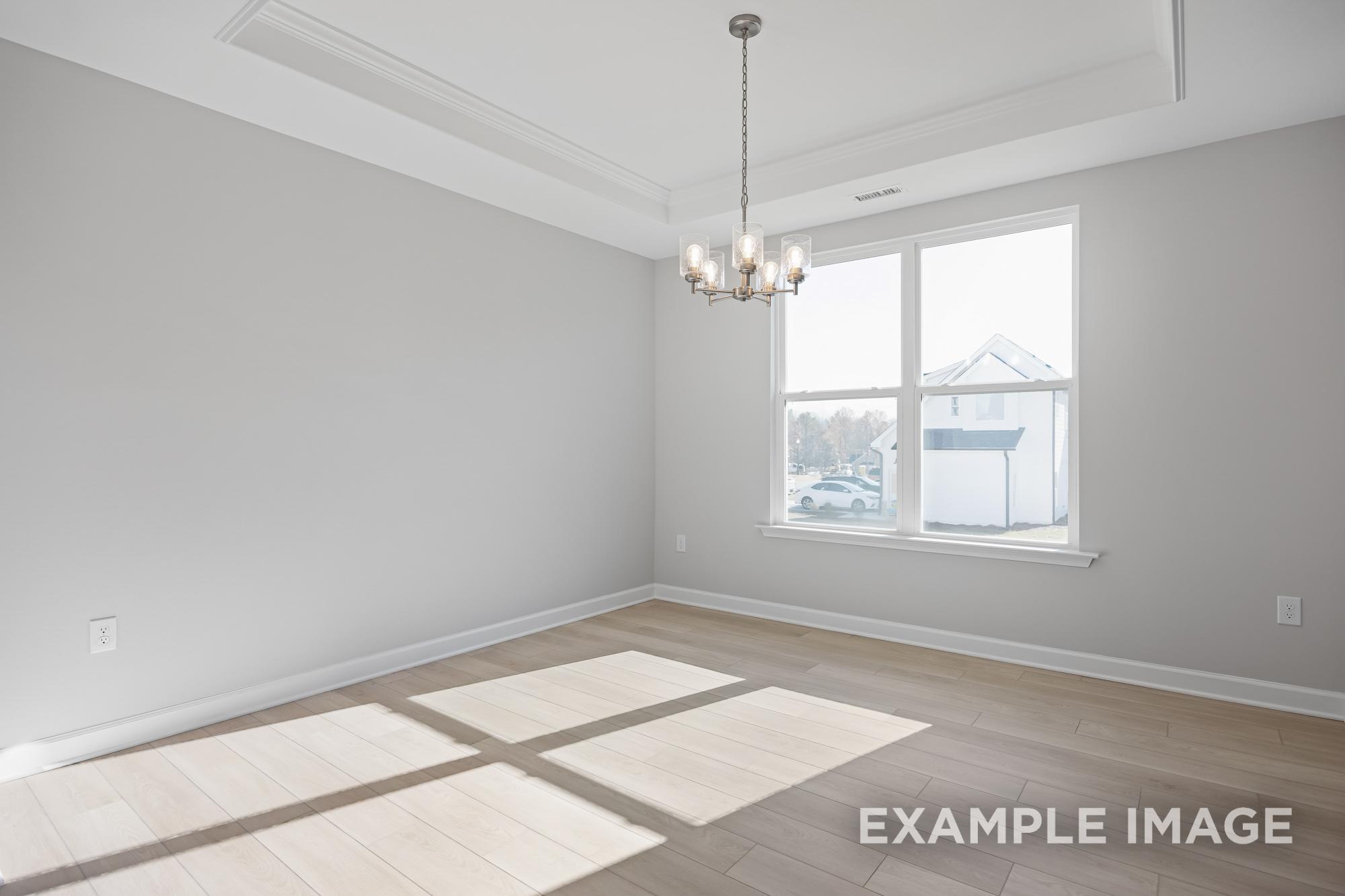 Spacious dining room interior in The Cypress B II with gray walls, chandelier, large windows, and sunlit hardwood floors
