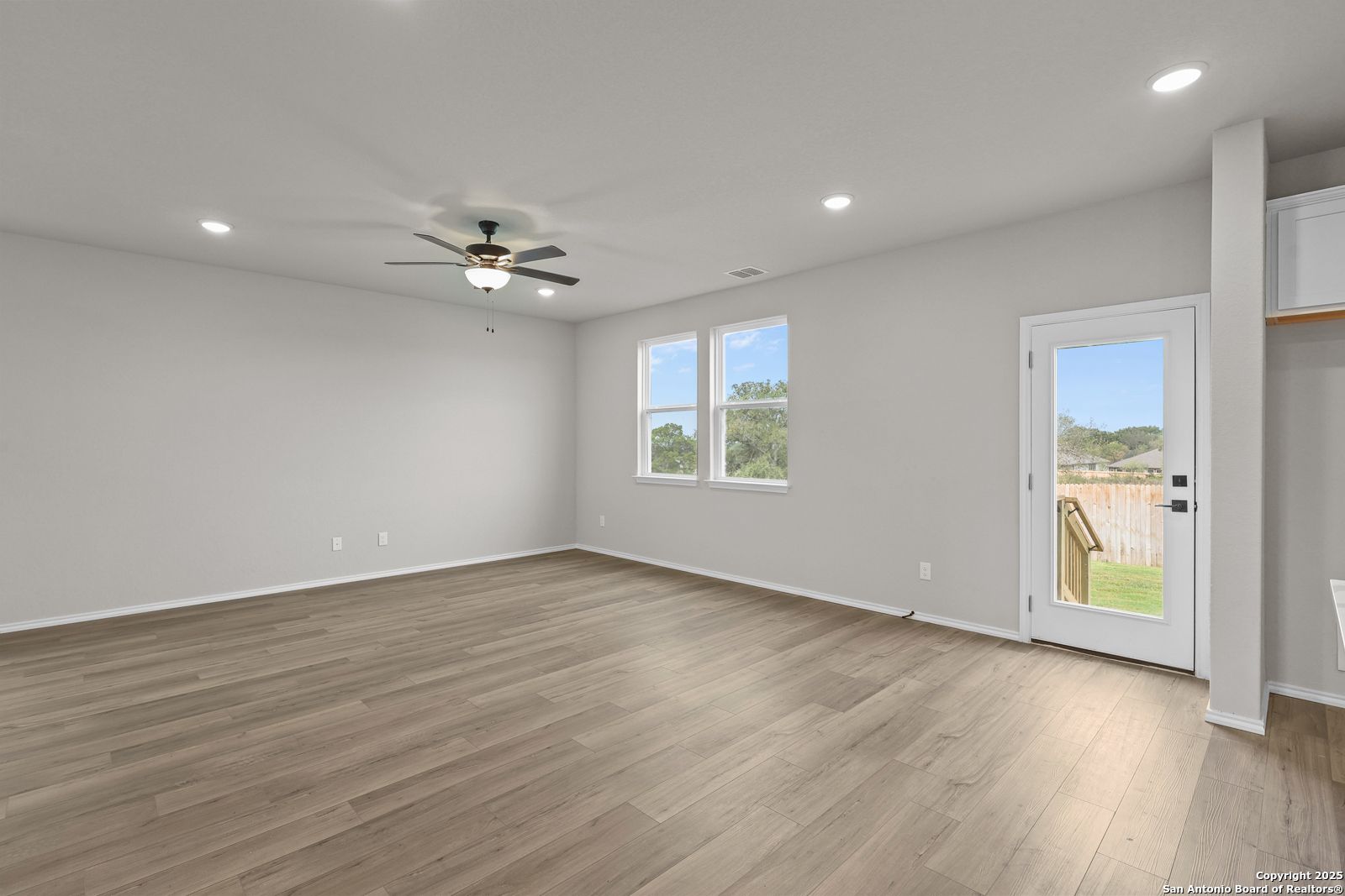 Spacious living room with hardwood floors, large windows, ceiling fan, and glass door to backyard in Davidson Homes The Murray J, San Antonio