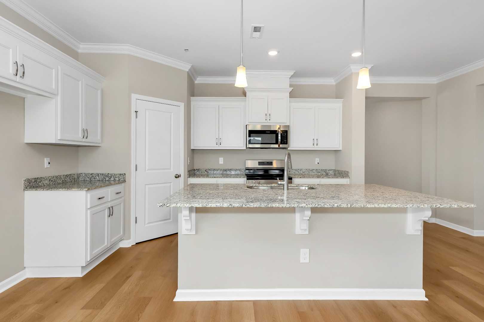 Spacious kitchen in The Orion home with white cabinets, granite island, stainless steel appliances, and hardwood floors