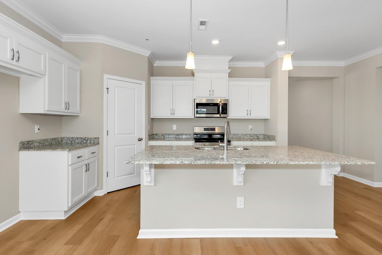 Spacious kitchen in The Orion home with white cabinets, granite island, stainless steel appliances, and hardwood floors