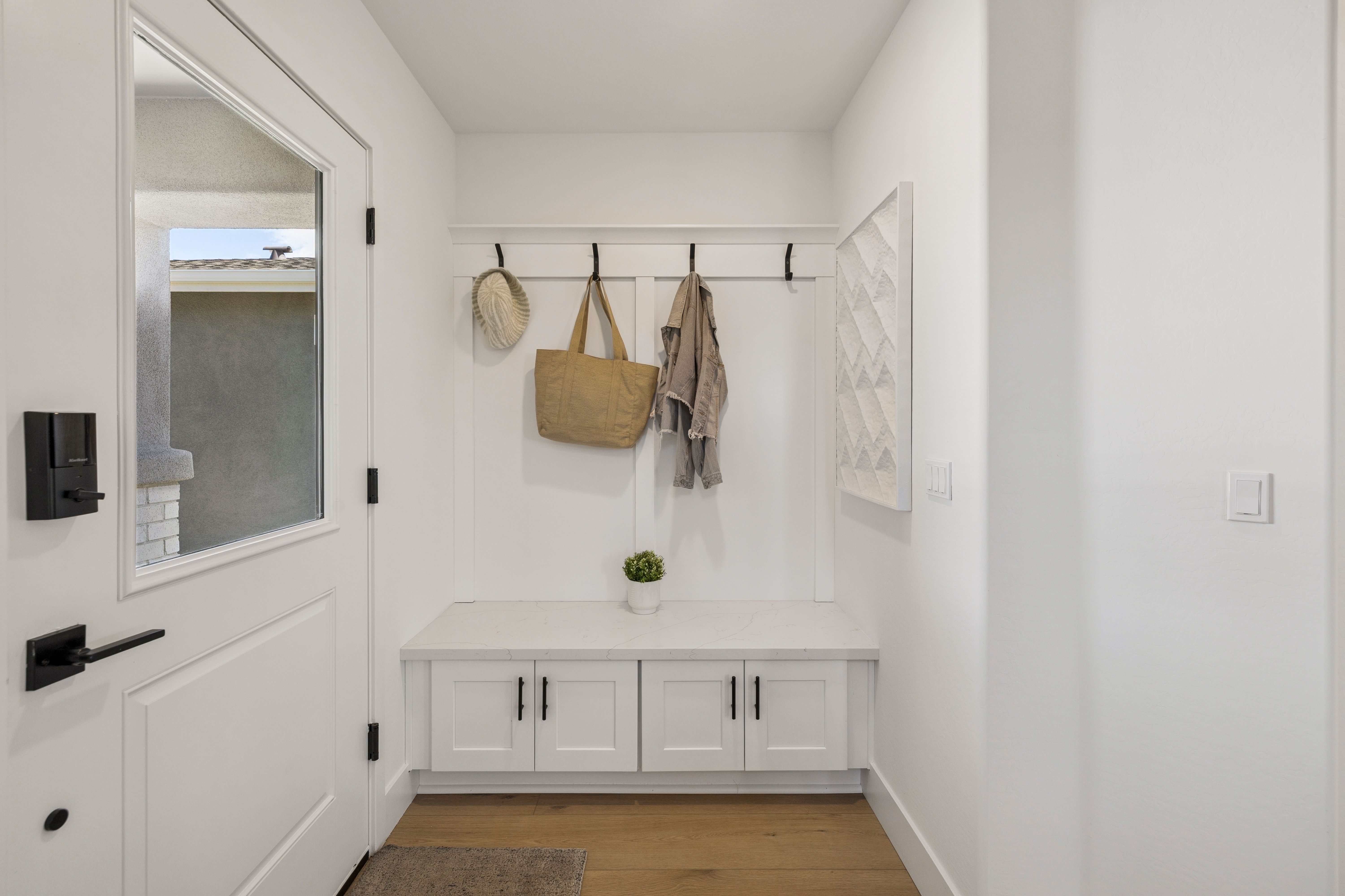Spacious white entryway mudroom at South Ranch Southern Collection in Prescott AZ featuring built-in bench, hooks with hat and bag, hardwood floors