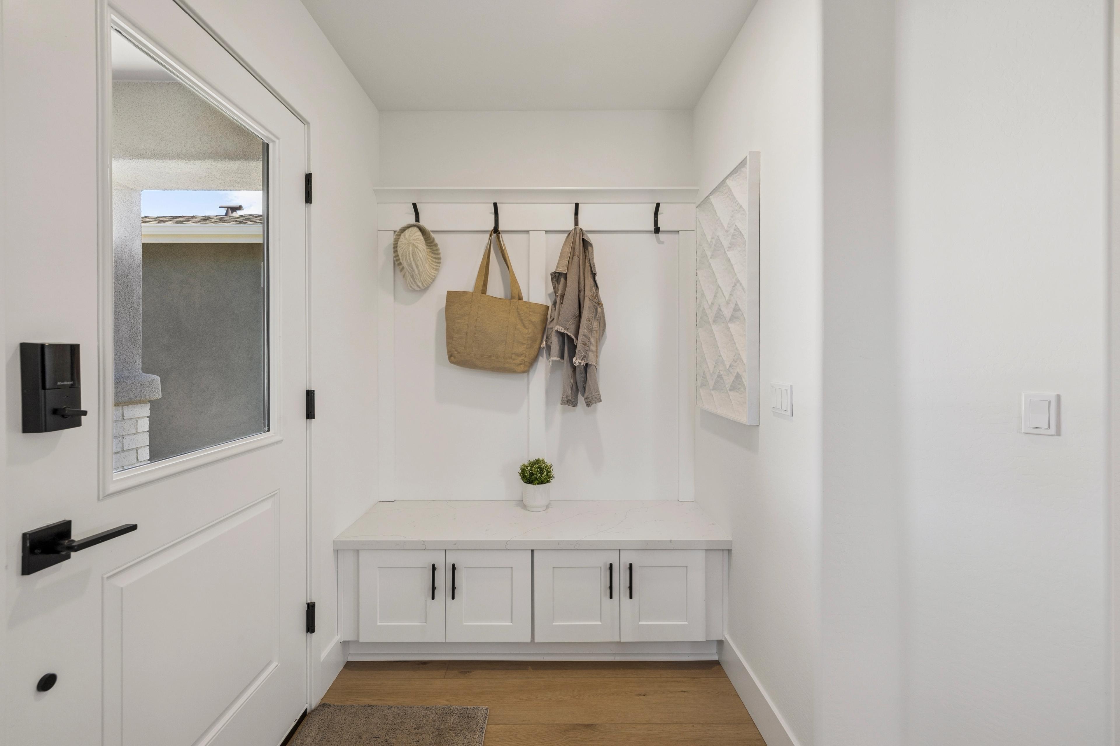 Spacious white entryway mudroom at South Ranch Southern Collection in Prescott AZ featuring built-in bench, hooks with hat and bag, hardwood floors