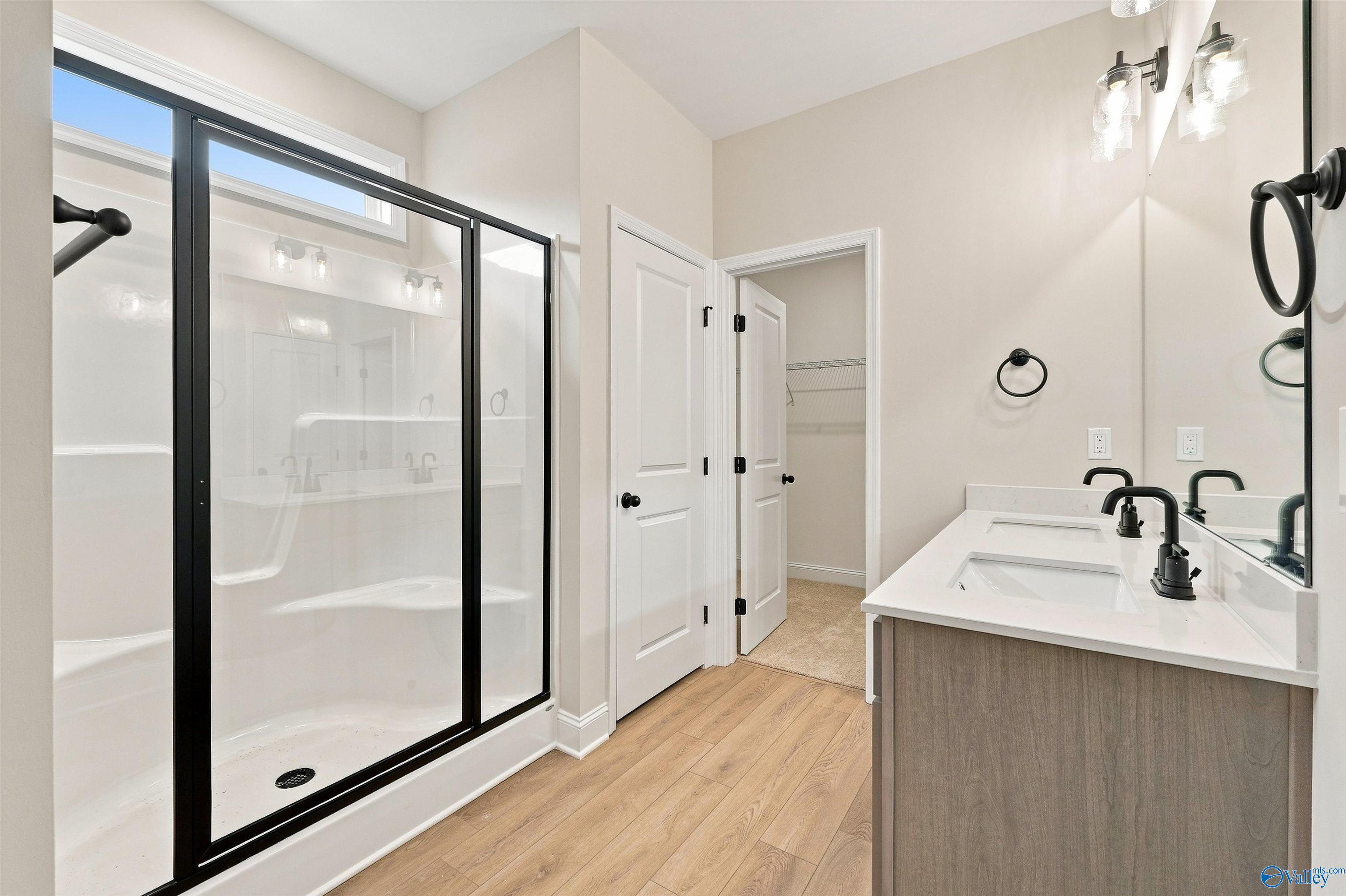 Master bathroom with black-framed shower, dual vanity, and hardwood floors in Davidson Homes The Franklin C, Athens, Alabama