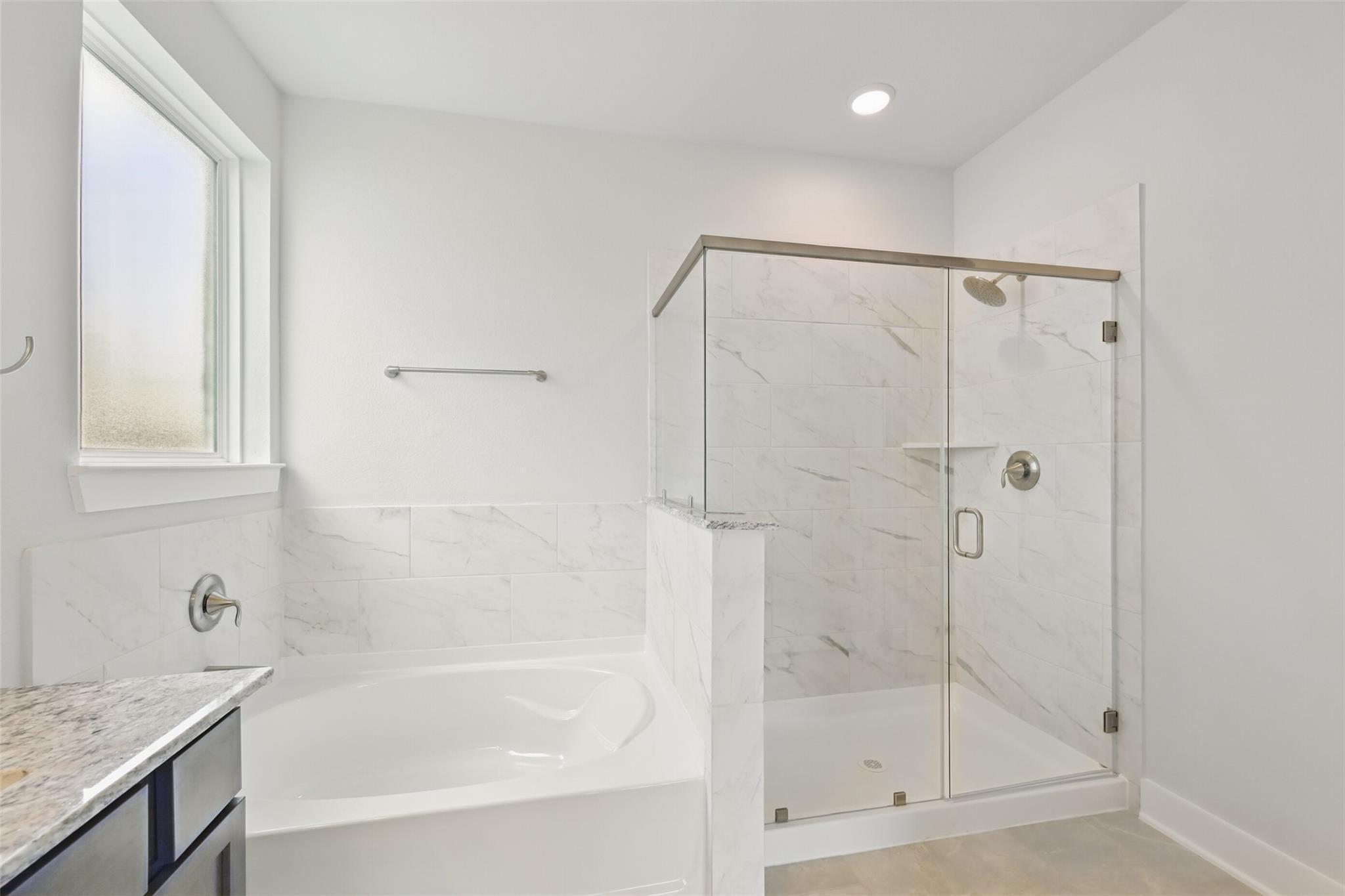 Elegant master bathroom with freestanding soaking tub, frameless glass shower, and marble tiles in Davidson Homes The Philip A, Lago Mar