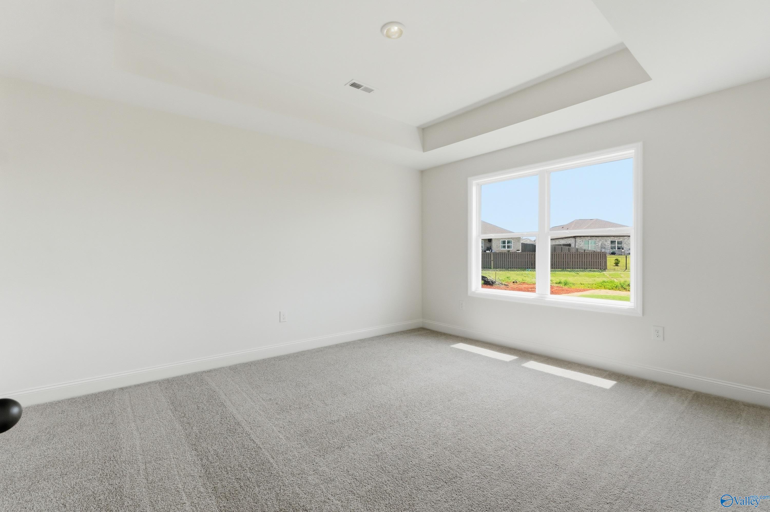 Bright bedroom with tray ceiling and carpet in The Franklin floor plan at Heritage Lakes, New Market, Alabama.