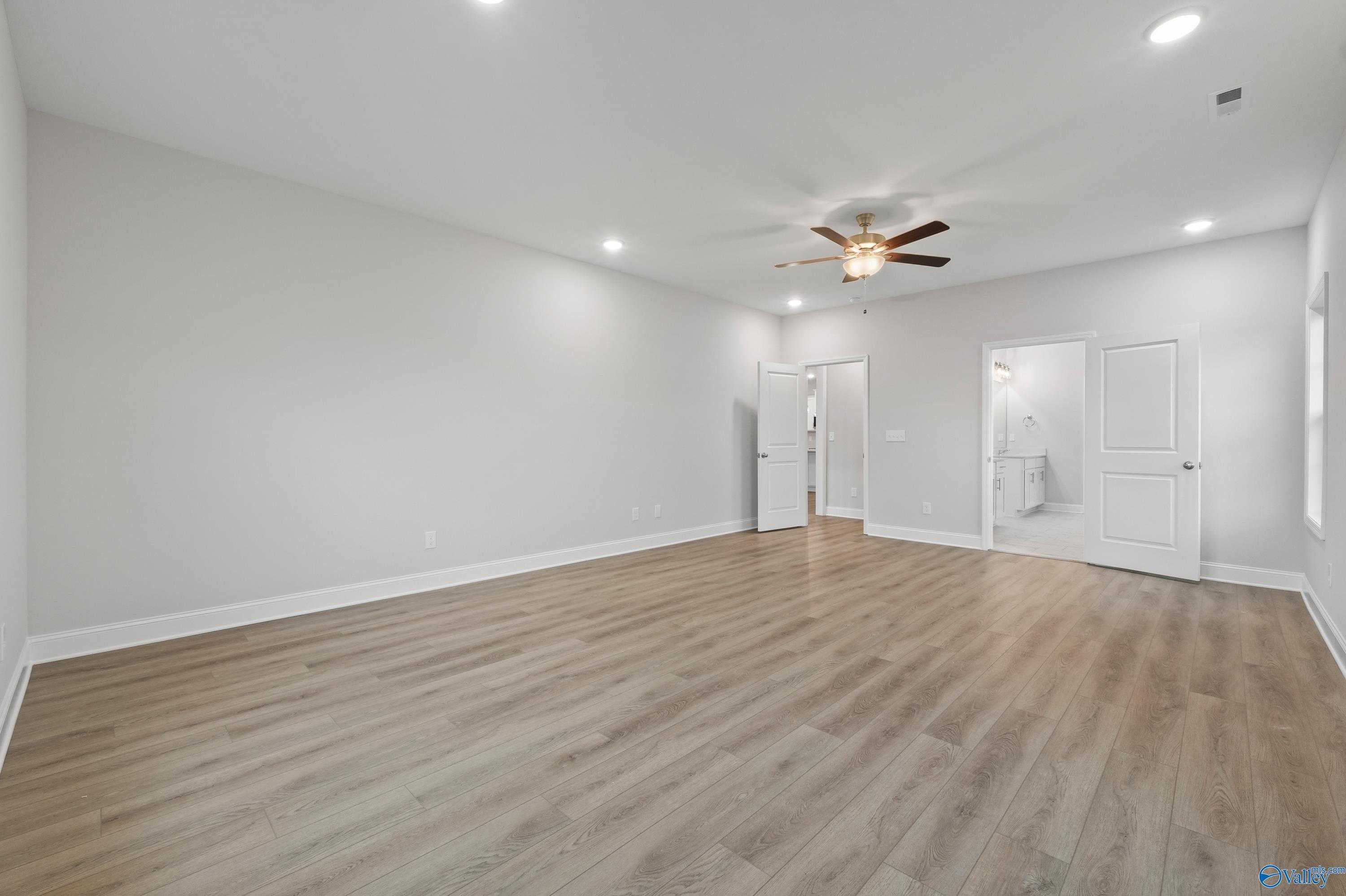 Spacious master bedroom with ceiling fan, light oak floors, and doors to walk-in closet and bathroom in Davidson Homes The Lanier, Harvest AL