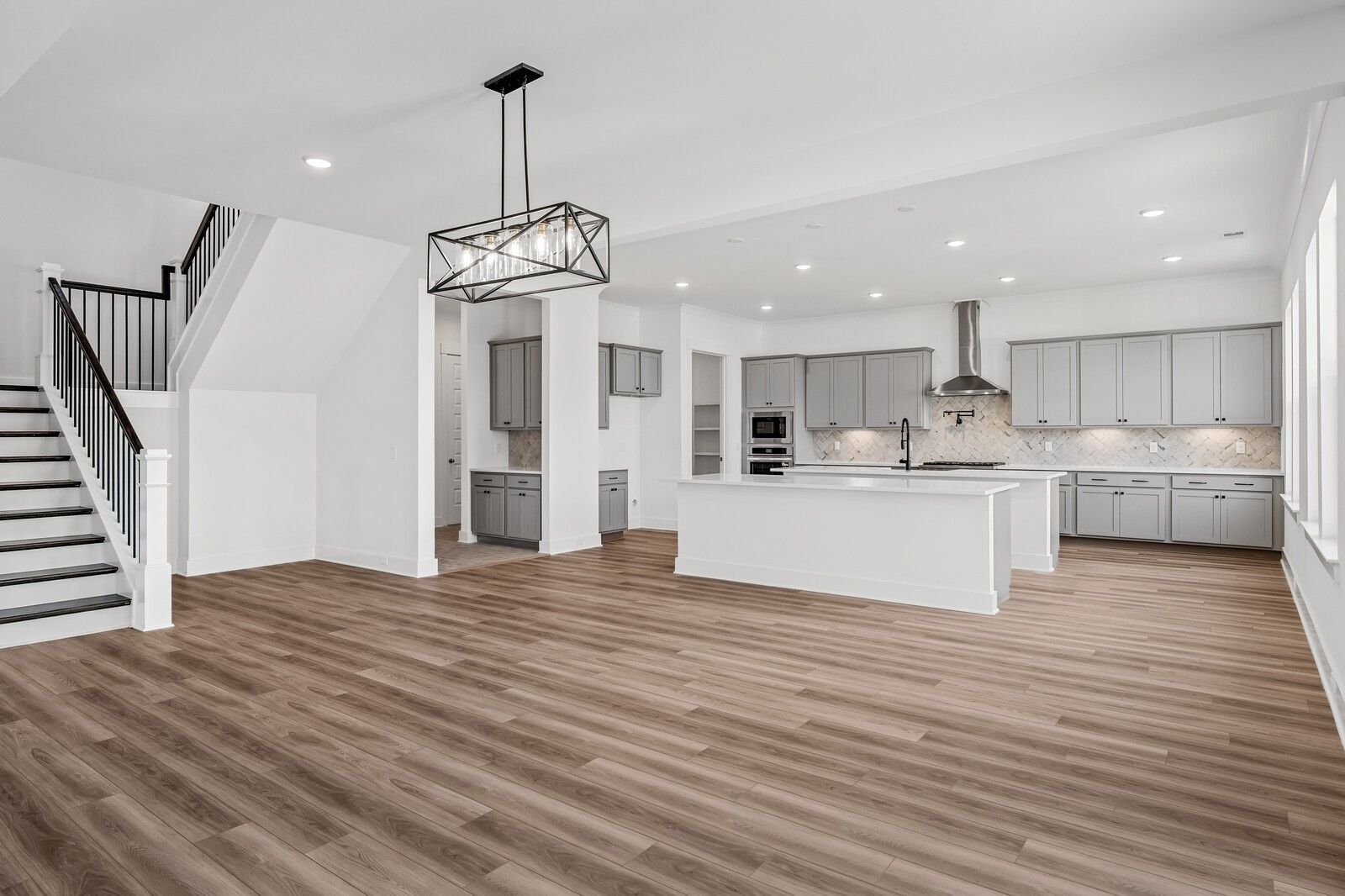 Open-concept kitchen and family room with white shaker cabinets, large island, stainless appliances, and hardwood floors in The Alston A, Murfreesboro, TN
