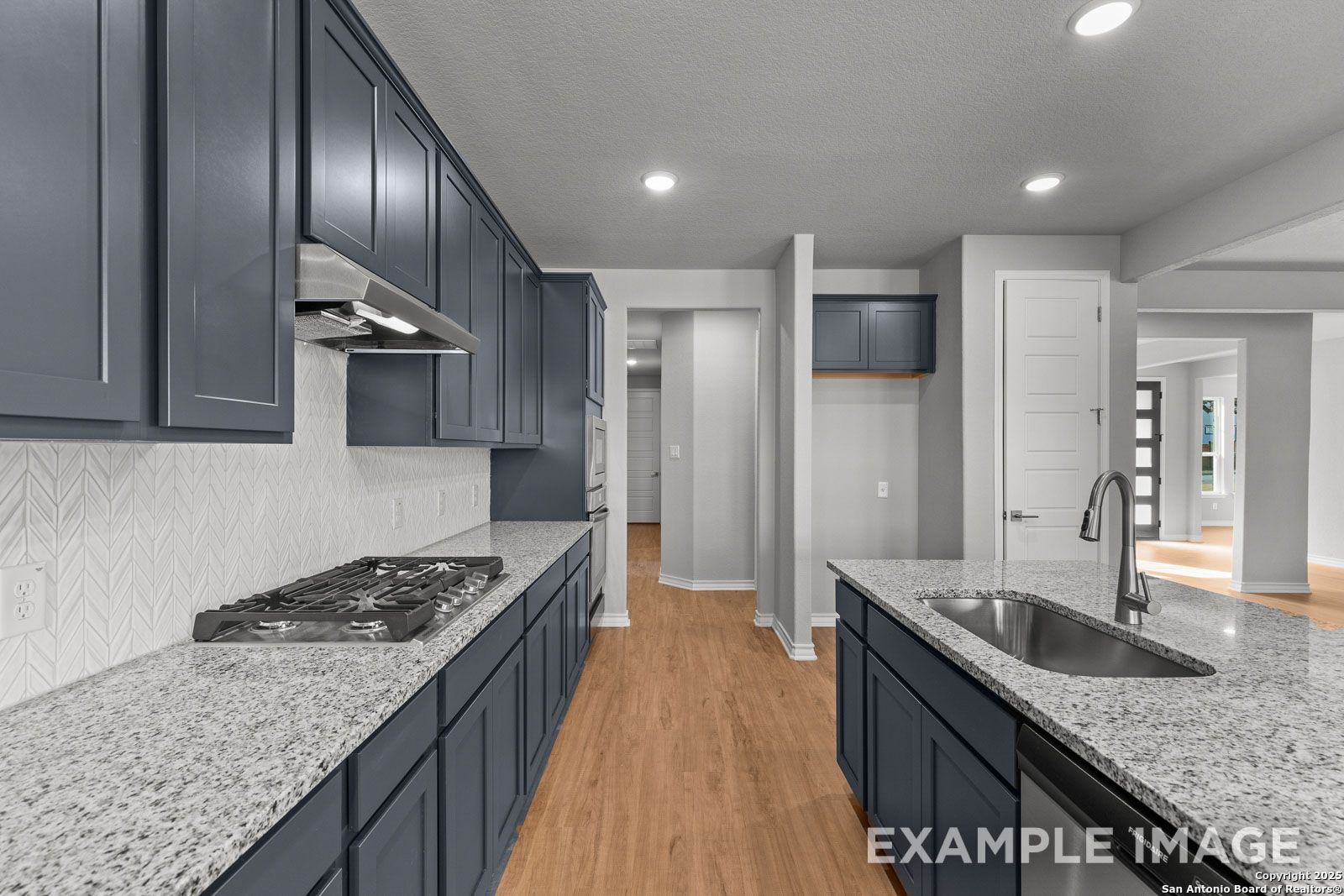 Modern kitchen in The Oxford featuring navy cabinets, granite countertops, and a center island in a Castroville, TX home.