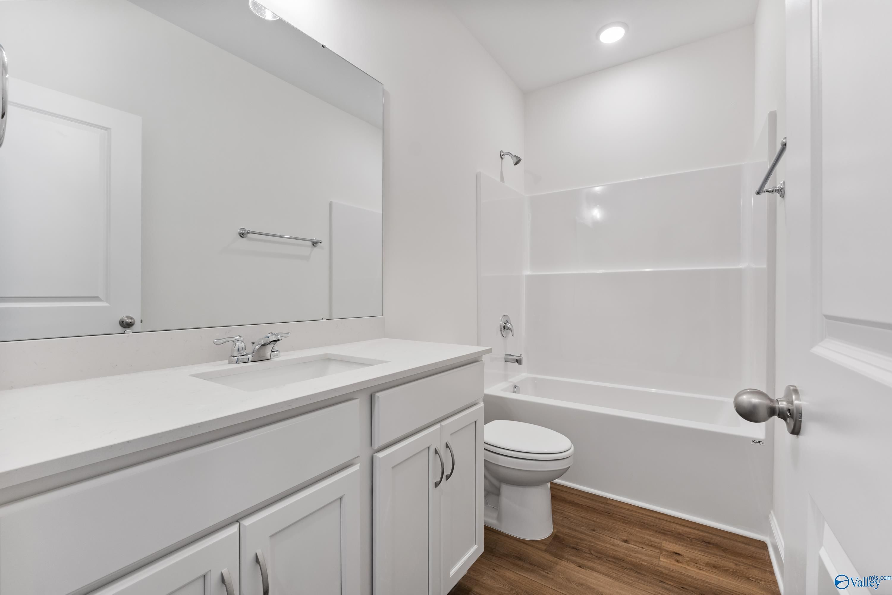 Bright white bathroom with bathtub-shower combo, glass enclosure, single vanity, and wood-look flooring in The Asheville C, New Market, Alabama