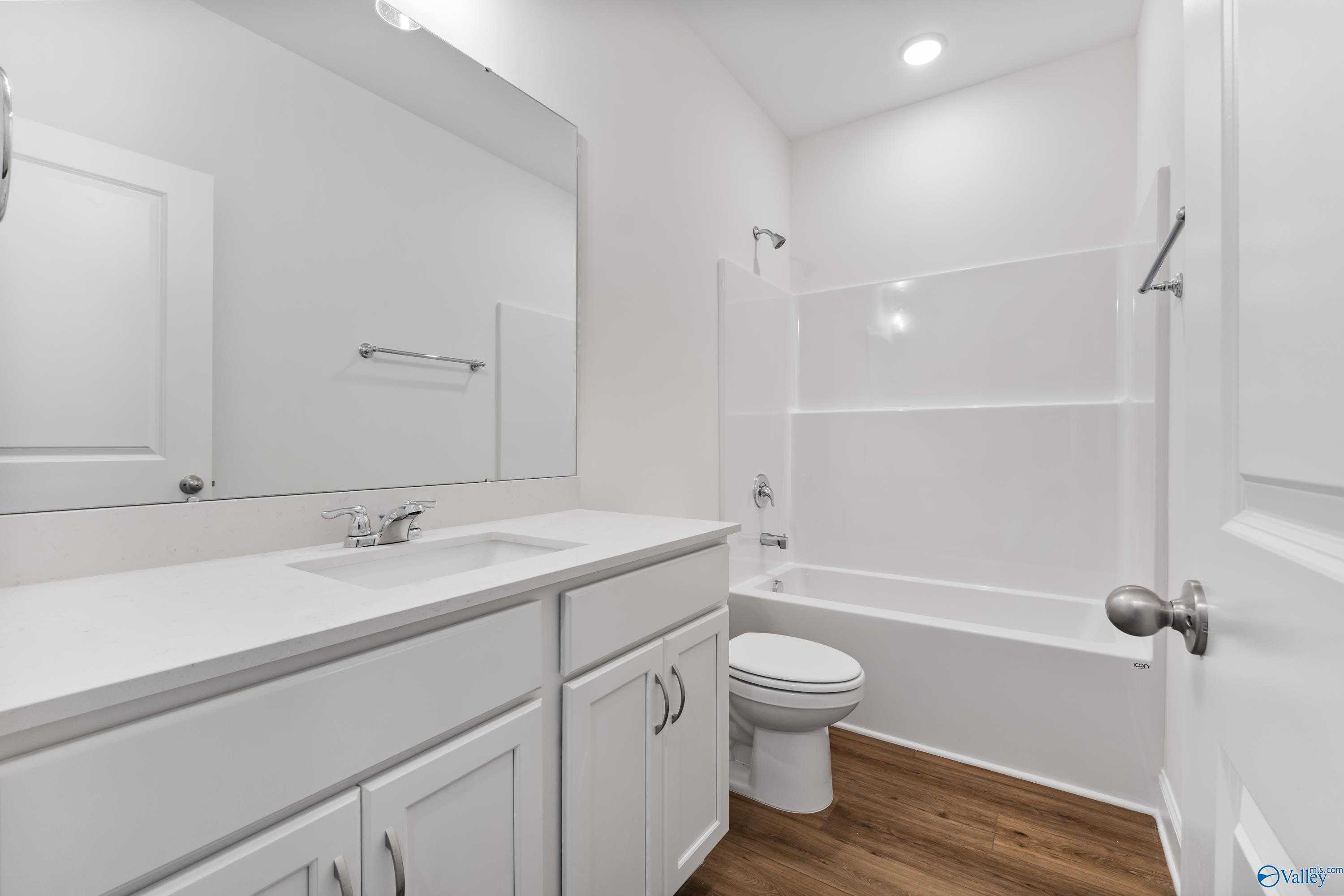 Bright white bathroom with bathtub-shower combo, glass enclosure, single vanity, and wood-look flooring in The Asheville C, New Market, Alabama